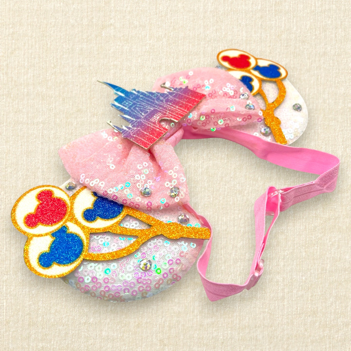 White sequin mouse ears with colorful mouse balloons and a pink bow with pastel pink and blue castle centerpiece on an elastic headband