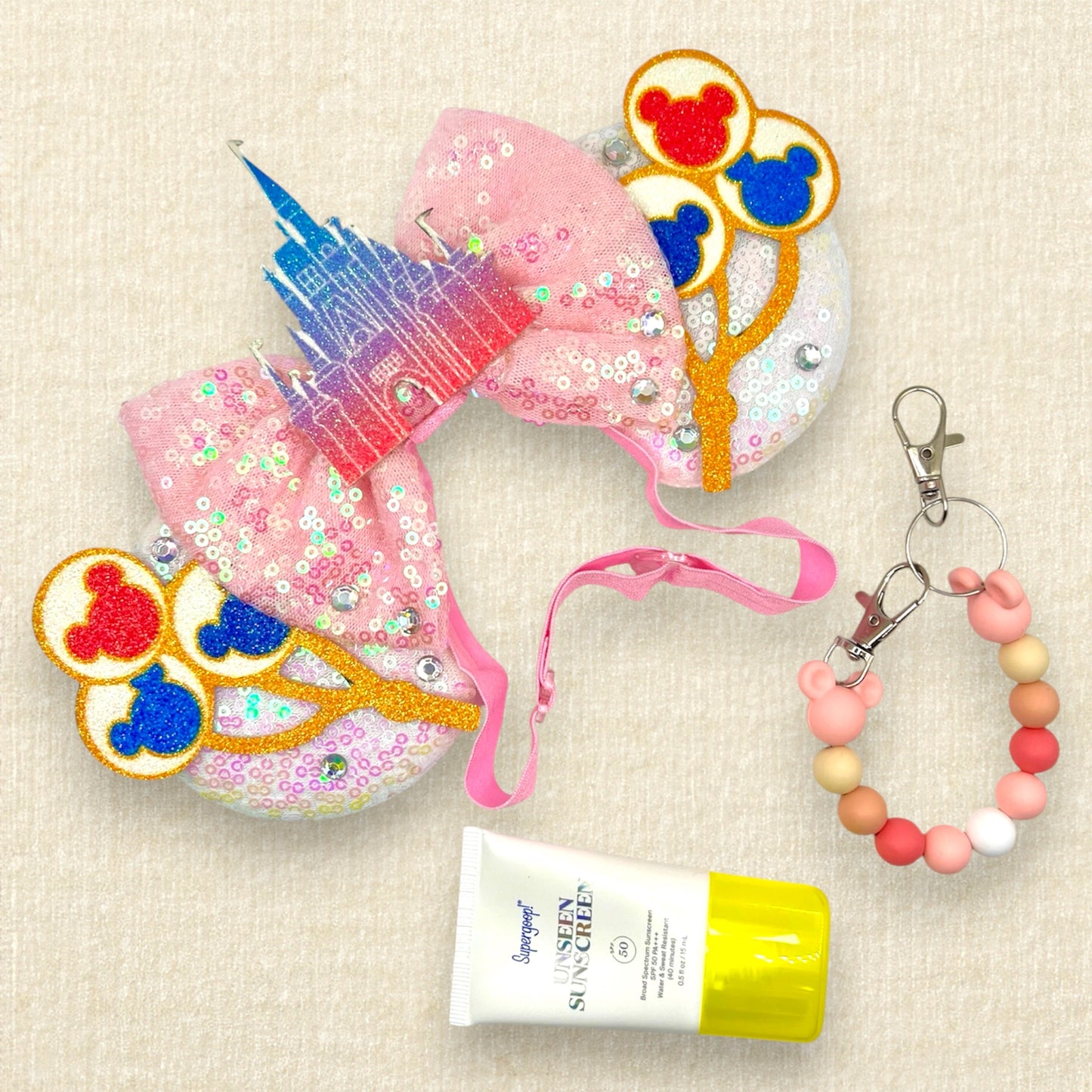 White sequin mouse ears with colorful mouse balloons and a pink bow with pastel pink and blue castle centerpiece on an elastic headband; sunscreen; and pink and white beaded mouse ears holder