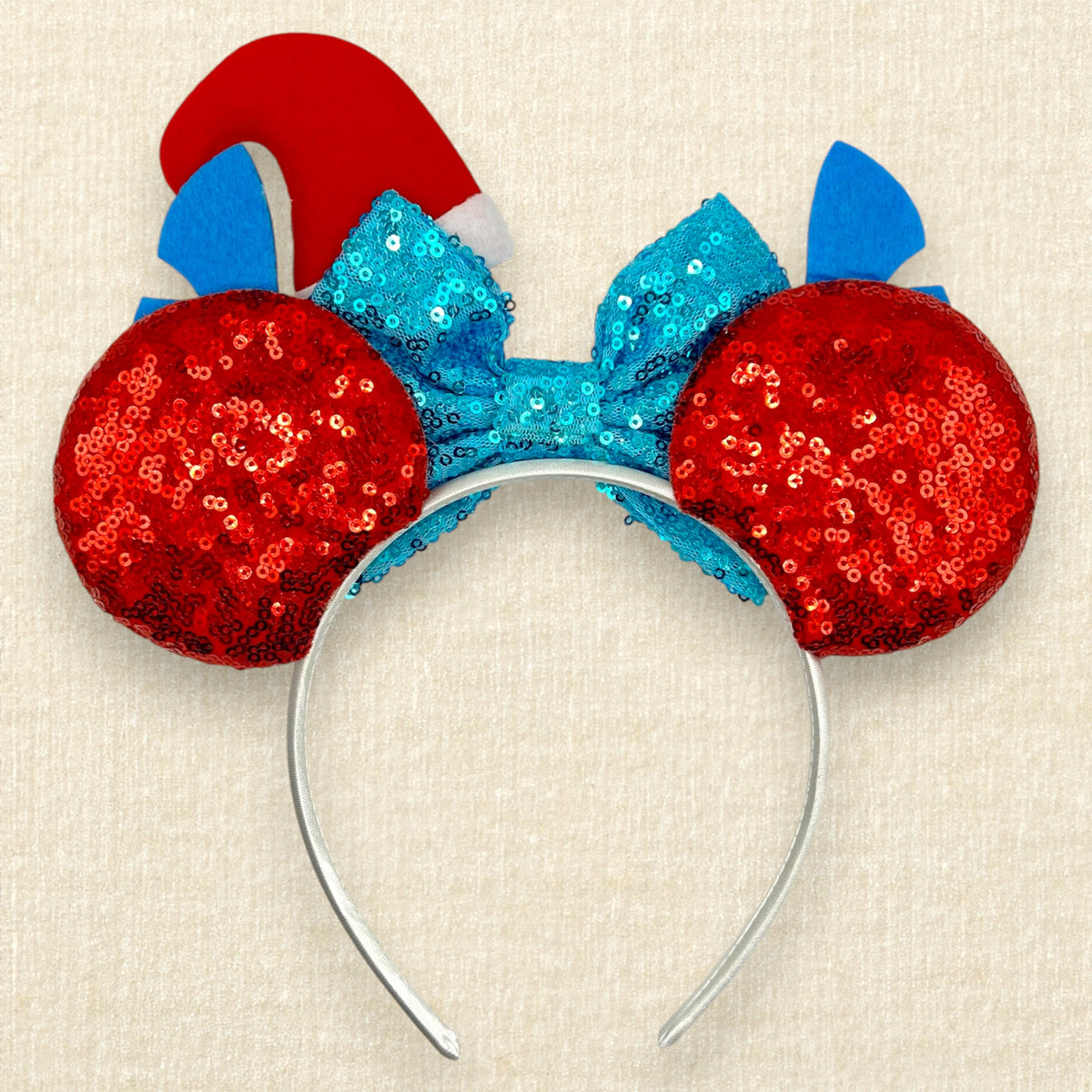 Christmas-themed mouse ears headband featuring a large sequined turquoise bow, red glitter mouse ears with white glitter palm leaves, blue and pink alien ears, and a red Santa hat with green holly (back view)