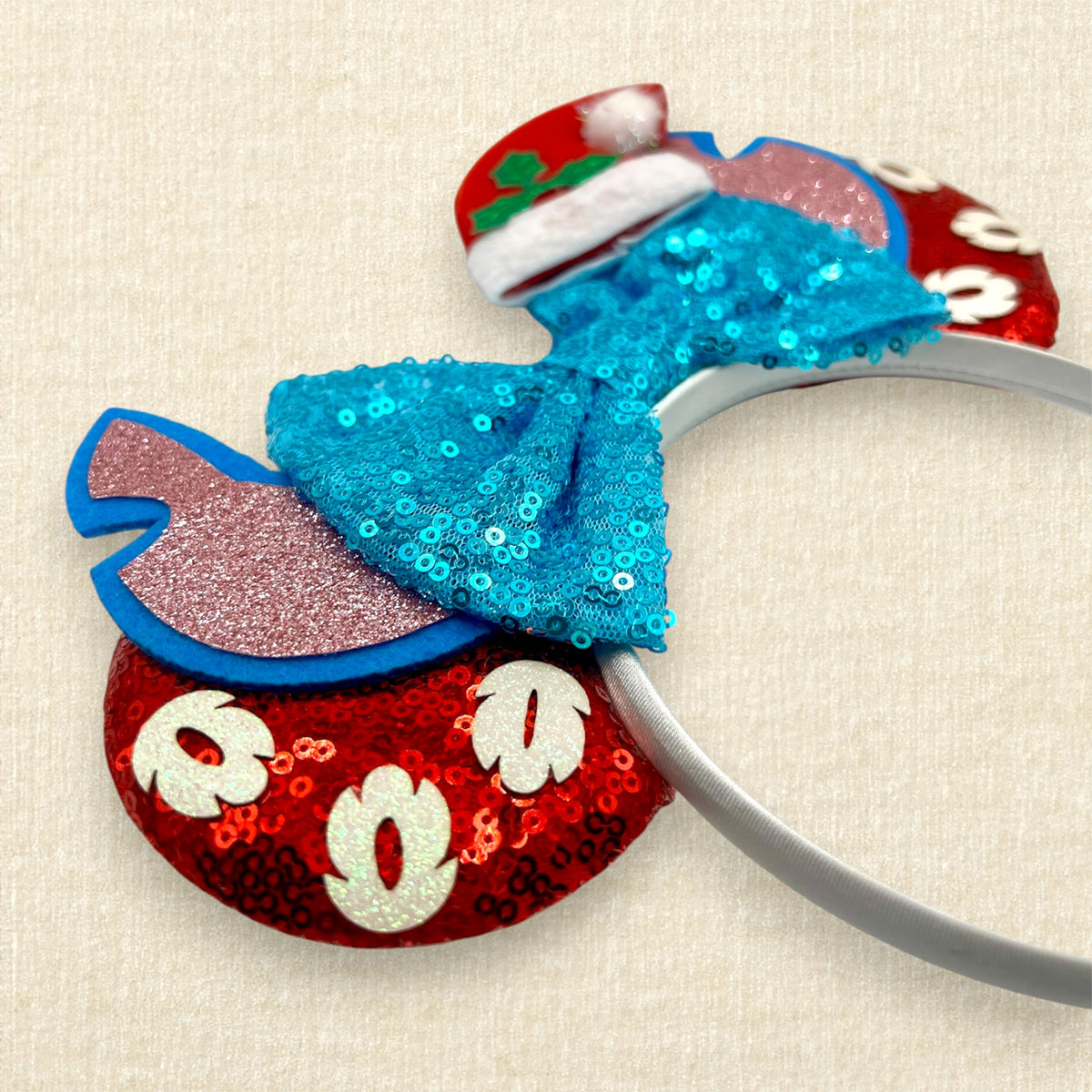 Christmas-themed mouse ears headband featuring a large sequined turquoise bow, red glitter mouse ears with white glitter palm leaves, blue and pink alien ears, and a red Santa hat with green holly.