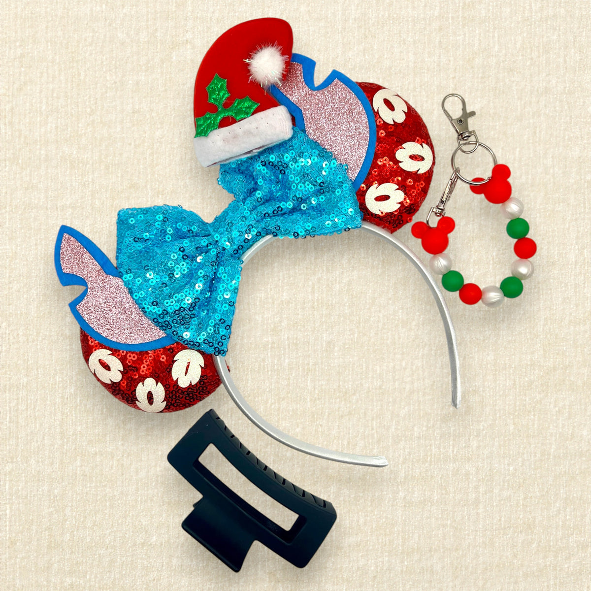 Christmas-themed mouse ears headband featuring a large sequined turquoise bow, red glitter mouse ears with white glitter palm leaves, blue and pink alien ears, and a red Santa hat with green holly; black claw clip; red, pearl white, and green beaded mouse ears holder keychain.
