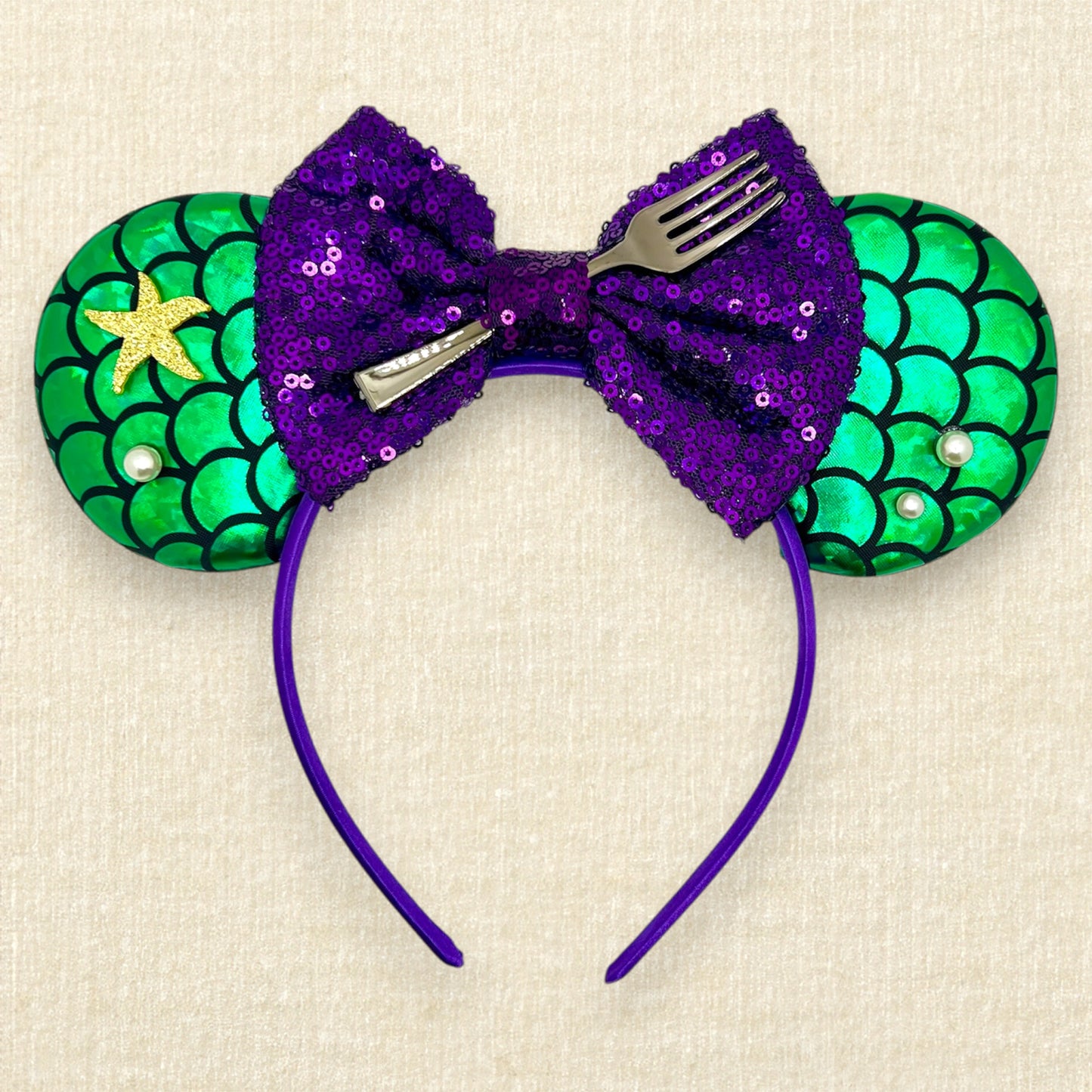 Mouse ears with a green iridescent scale pattern with purple bow, pearls, glitter starfish, and silver fork centerpiece