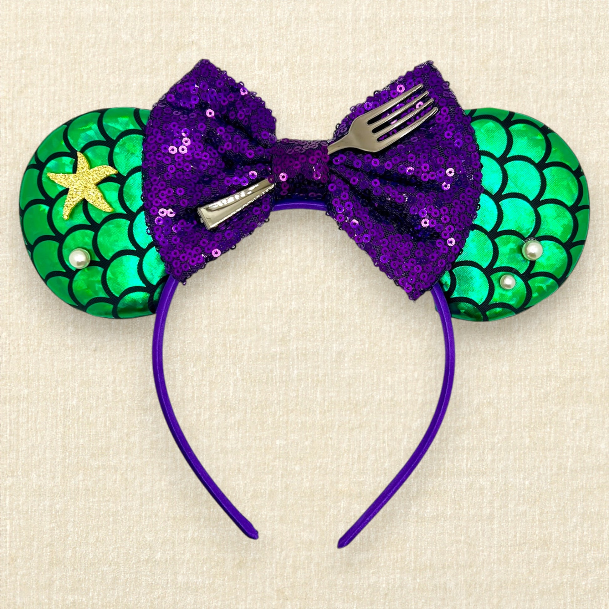 Mouse ears with a green iridescent scale pattern with purple bow, pearls, glitter starfish, and silver fork centerpiece