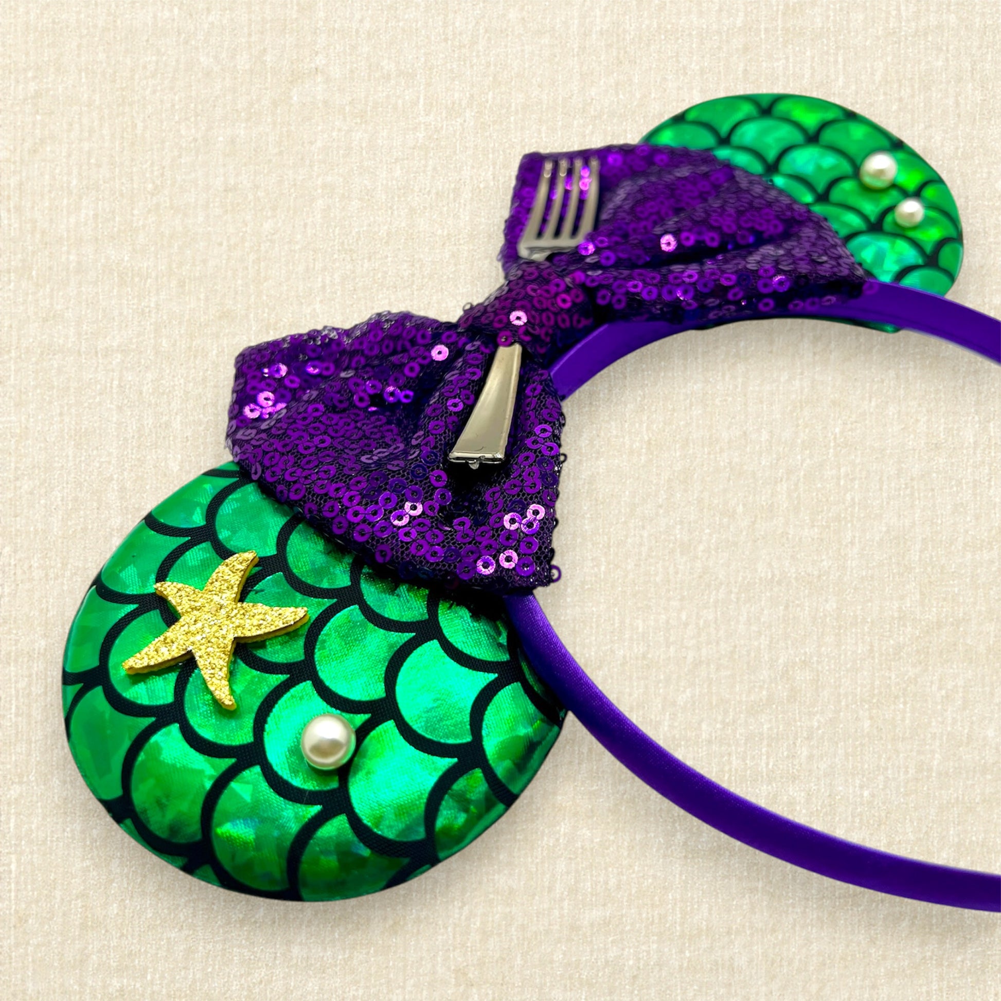 Mouse ears with a green iridescent scale pattern with purple bow, pearls, glitter starfish, and silver fork centerpiece