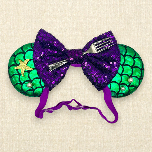 Mouse ears with a green iridescent scale pattern with purple bow, pearls, glitter starfish, and silver fork on an elastic headband