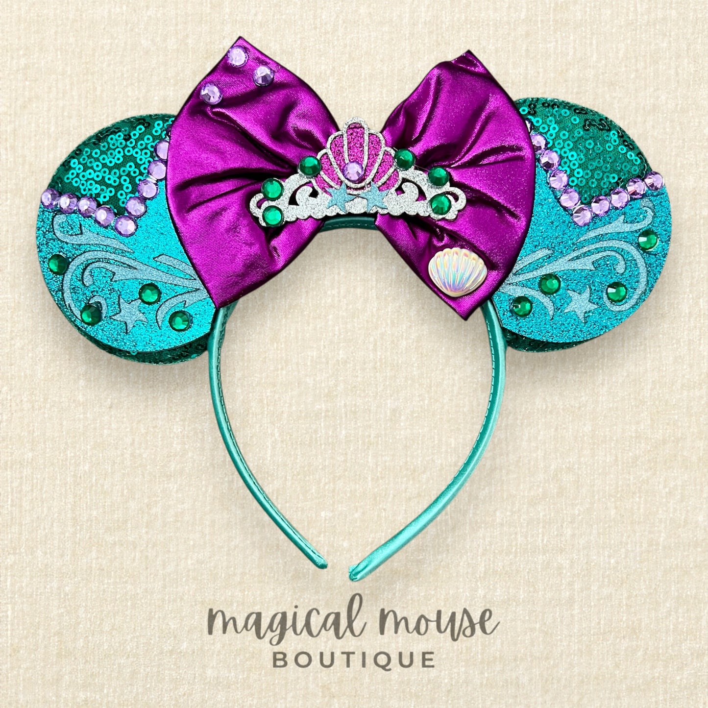 Green and purple mermaid-themed mouse ears headband on a beige background, branded 'magical mouse boutique' 