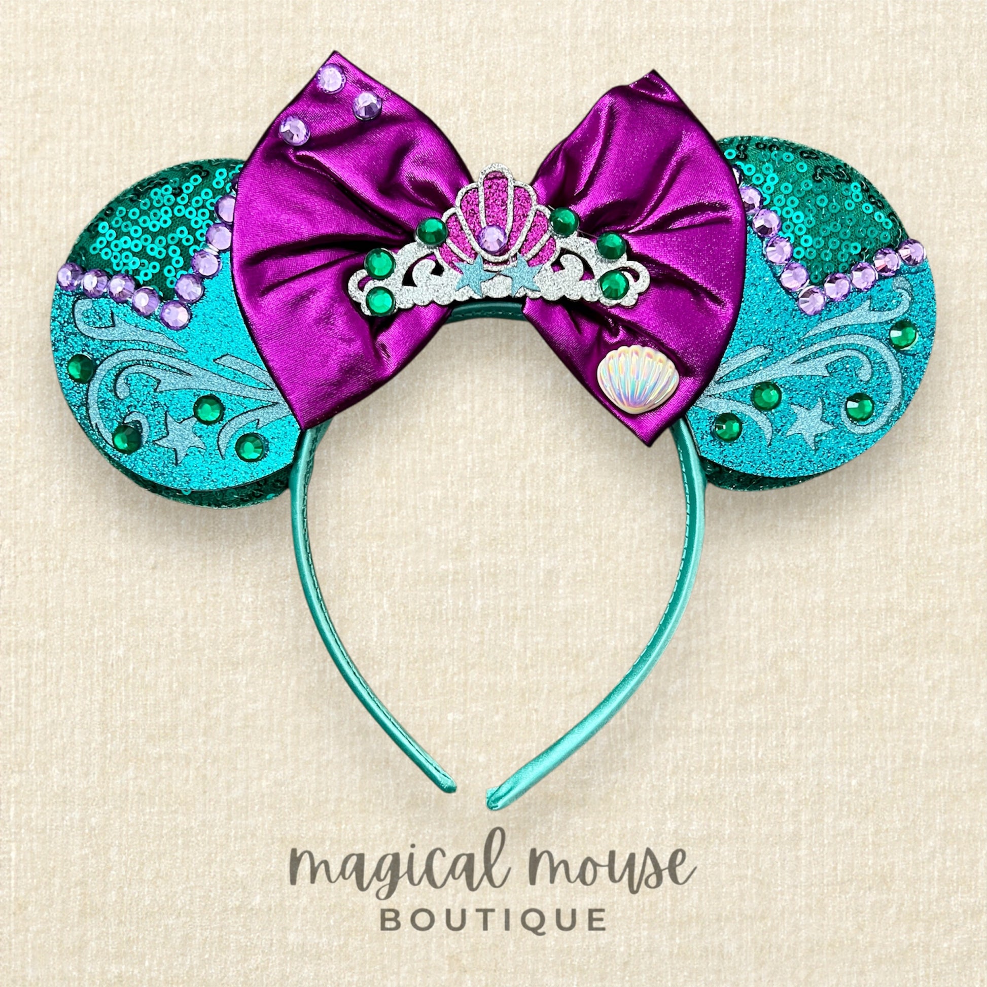 Green and purple mermaid-themed mouse ears headband on a beige background, branded 'magical mouse boutique' 