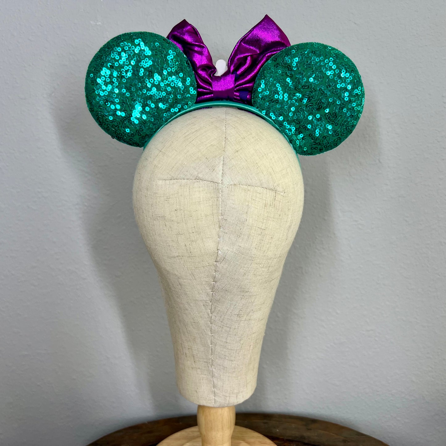 Green and purple mermaid-themed mouse ears headband on a mannequin head