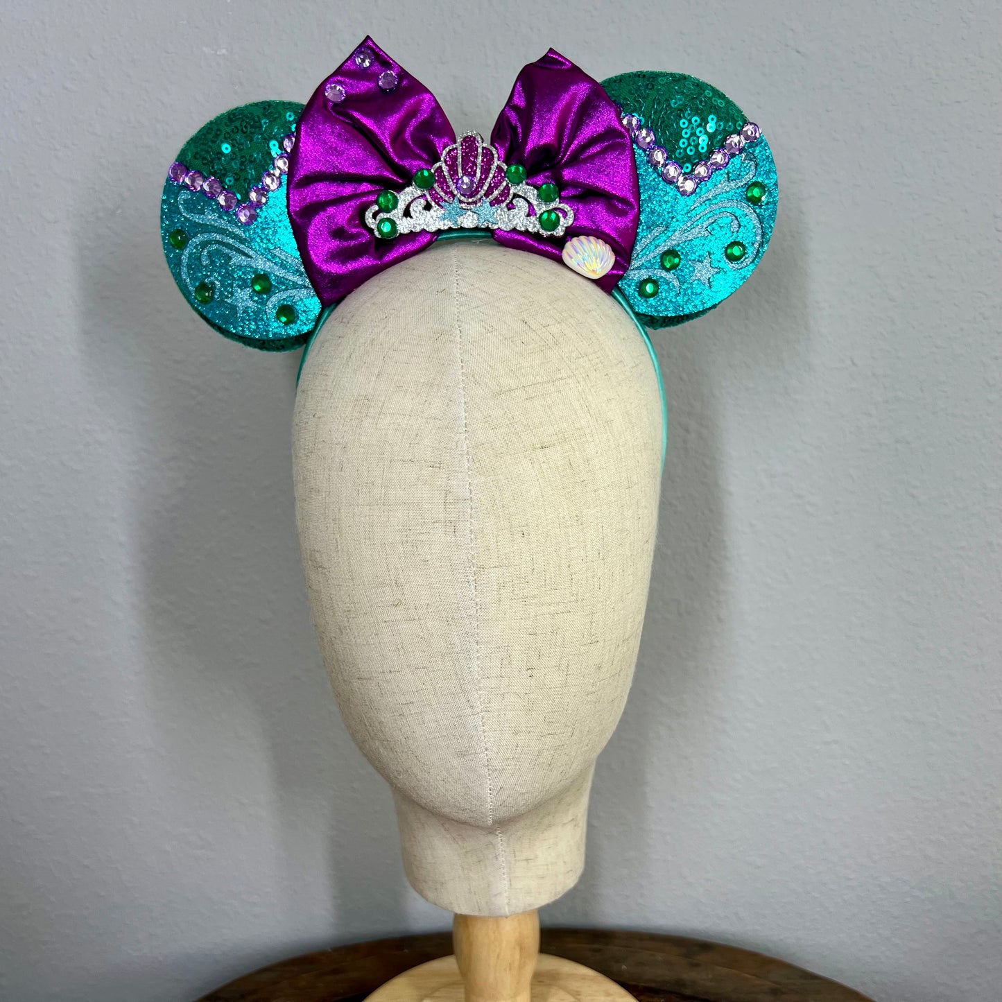 Green and purple mermaid-themed mouse ears headband on a mannequin head