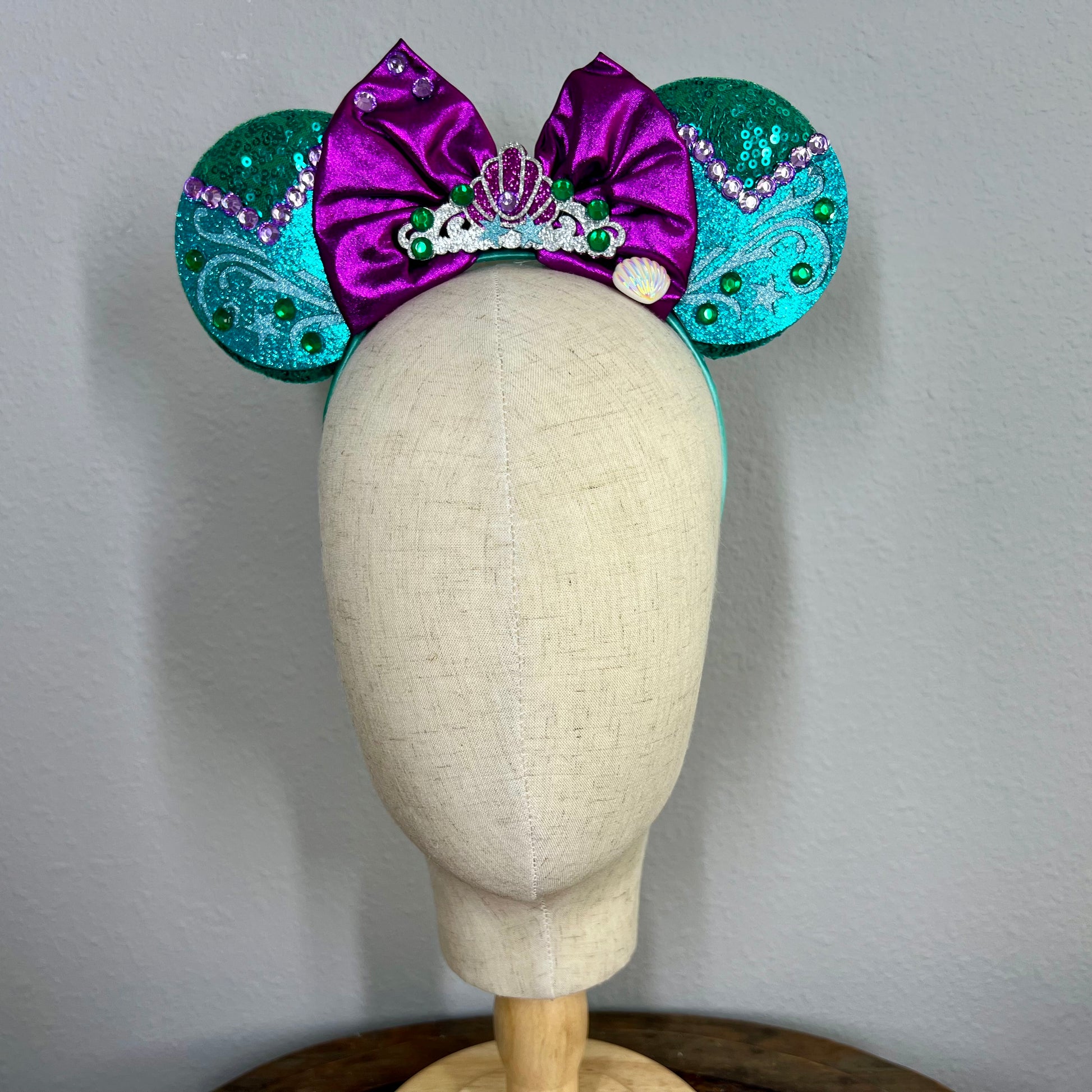Green and purple mermaid-themed mouse ears headband on a mannequin head