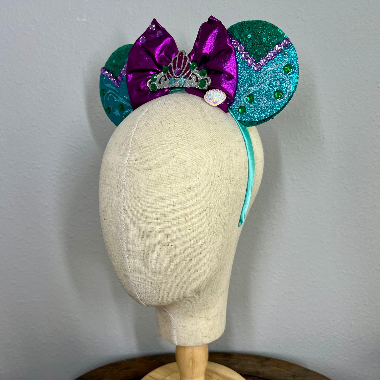 Green and purple mermaid-themed mouse ears headband on a mannequin head
