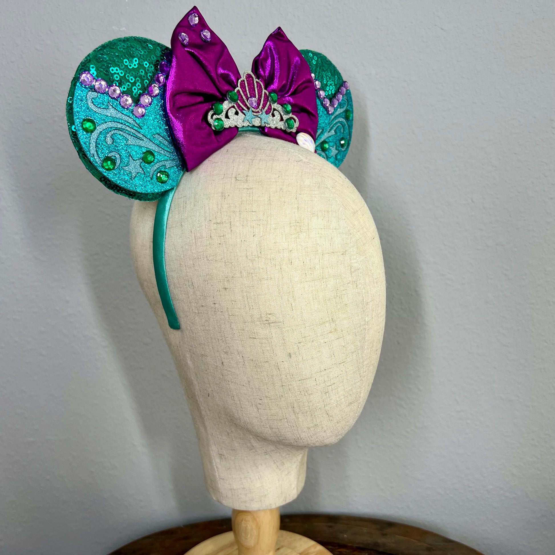 Green and purple mermaid-themed mouse ears headband on a mannequin head