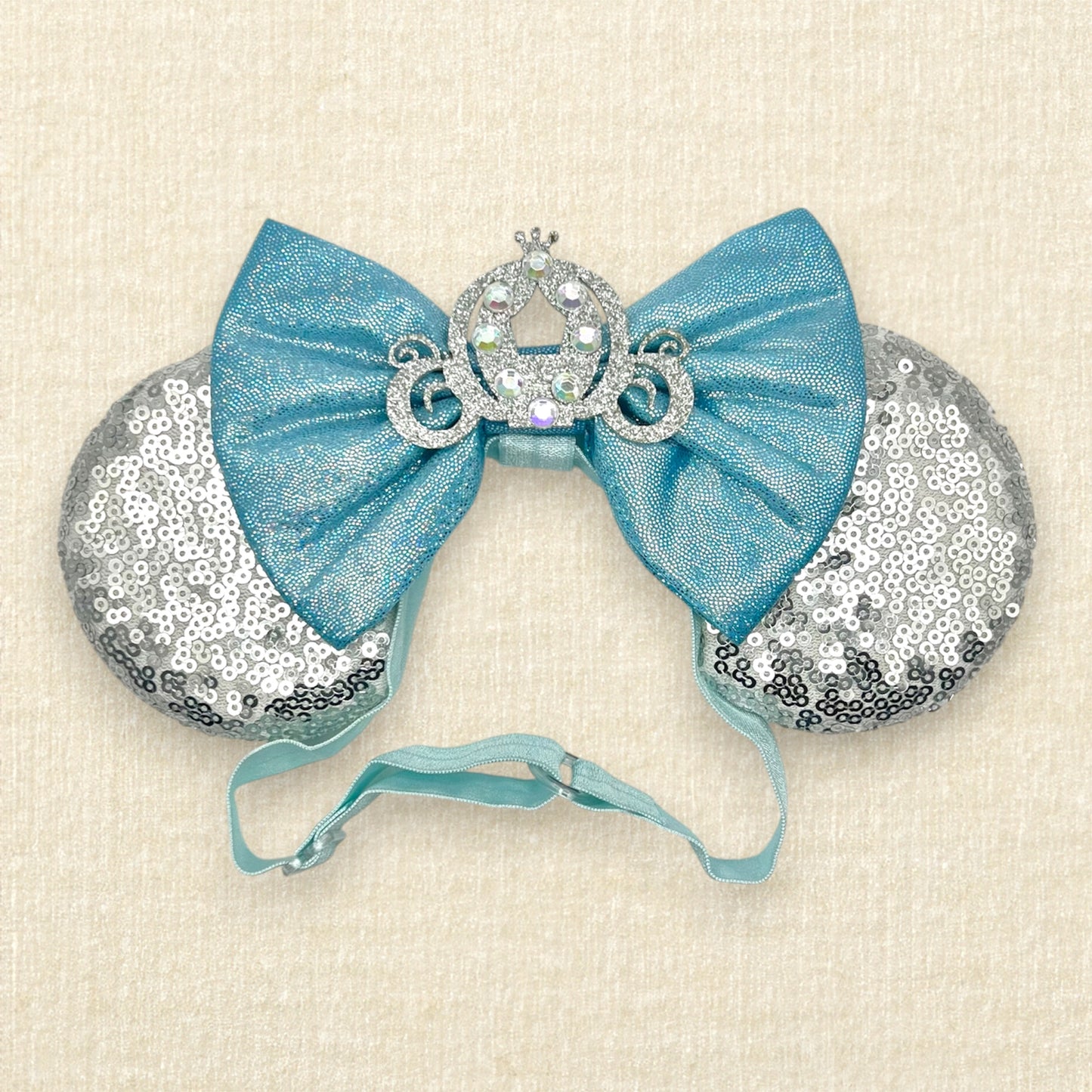 Silver sequin mouse ears on an elastic headband with shimmery blue bow and silver glitter carriage accent and rhinestones