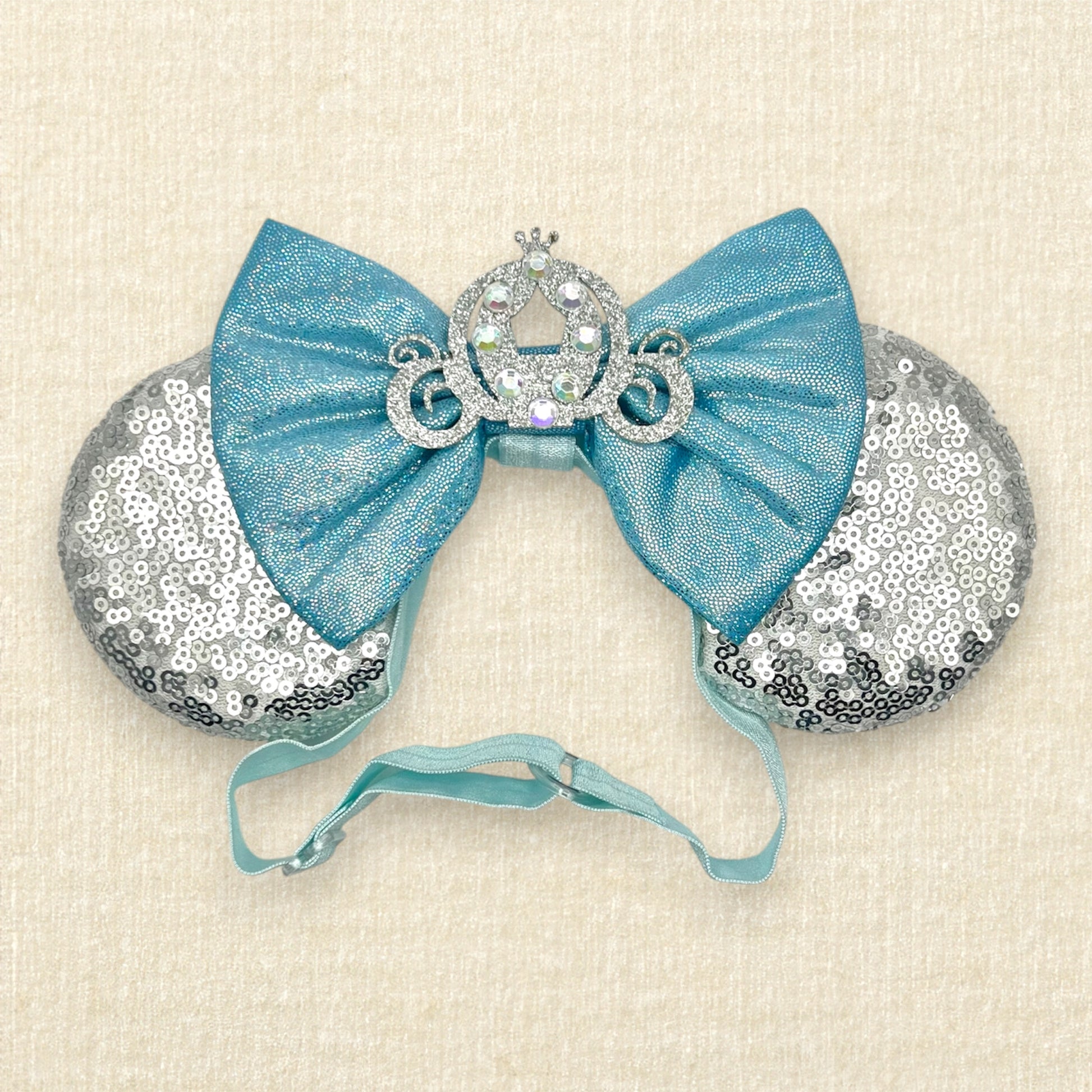 Silver sequin mouse ears on an elastic headband with shimmery blue bow and silver glitter carriage accent and rhinestones