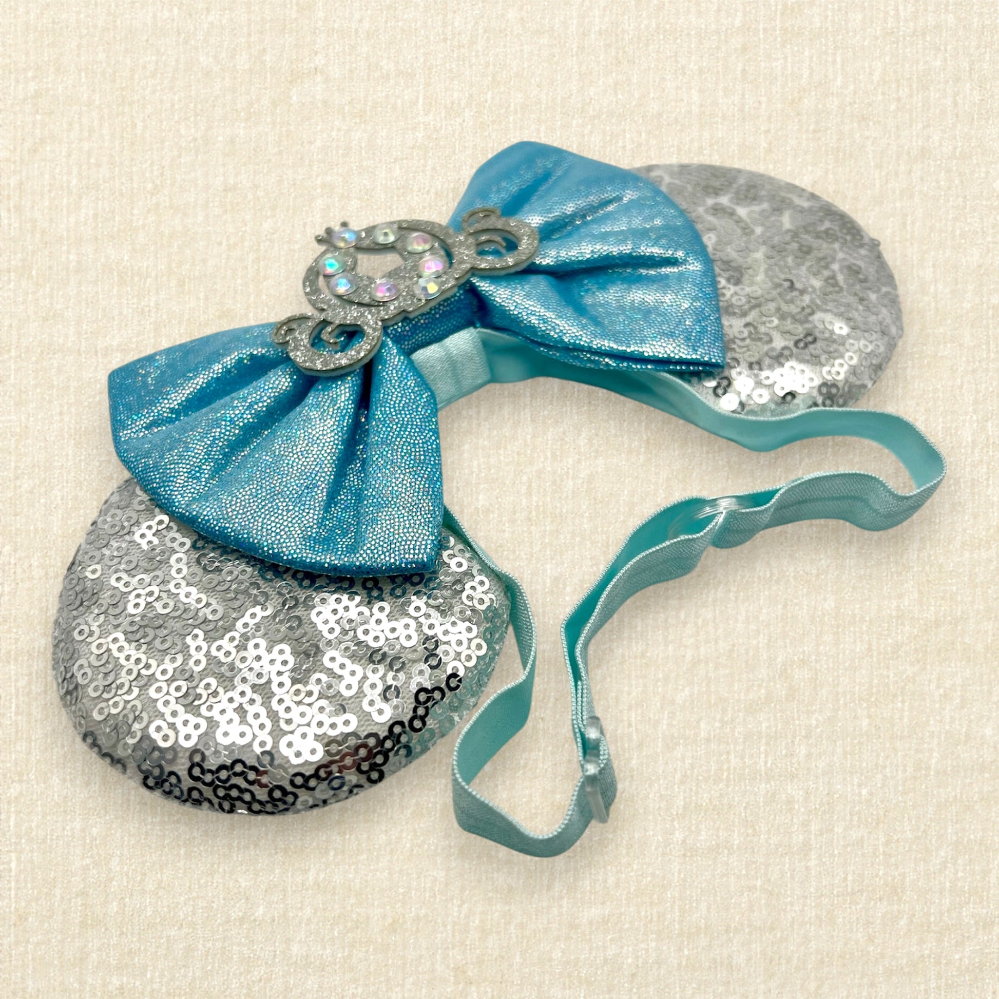 Silver sequin mouse ears on an elastic headband with shimmery blue bow and silver glitter carriage accent and rhinestones