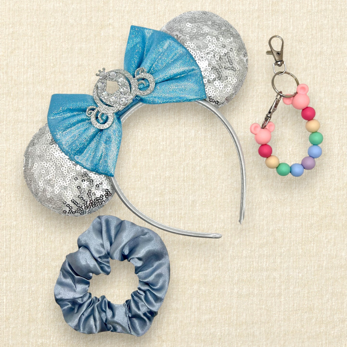 Silver sequin mouse ears with shimmery blue bow, silver glitter carriage accent, and rhinestones; blue scrunchie; colorful rainbow beaded mouse ears holder