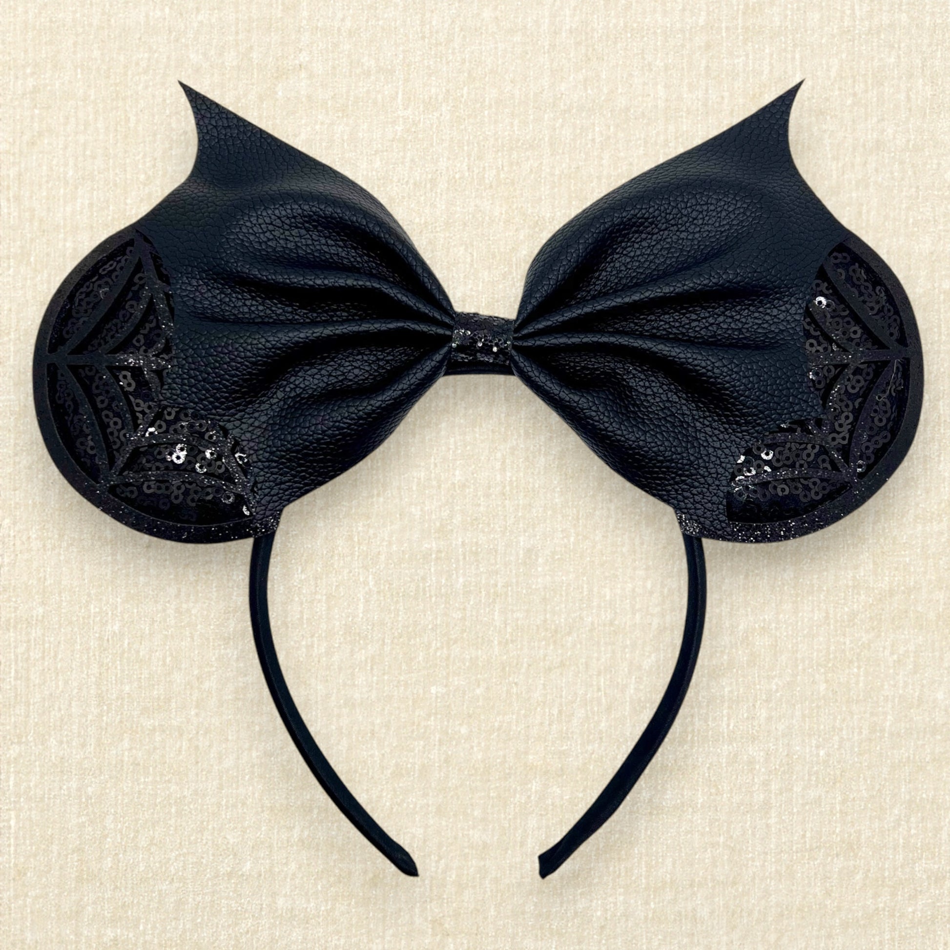 Halloween-themed mouse ears headband with black sequin ears, black glitter cobwebs, and black bat wing faux leather bow