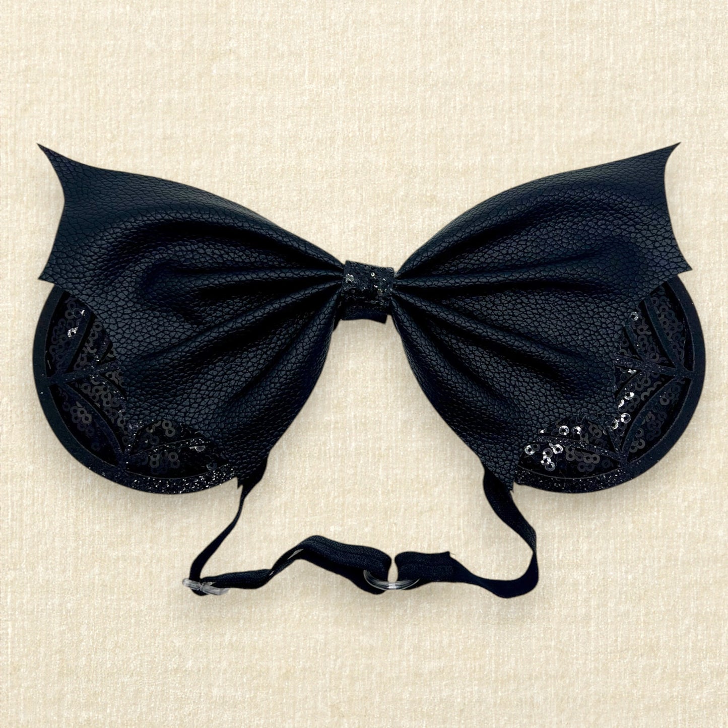 Halloween-themed mouse ears with black sequin ears, black glitter cobwebs, and black faux leather bat wing bow on an elastic headband