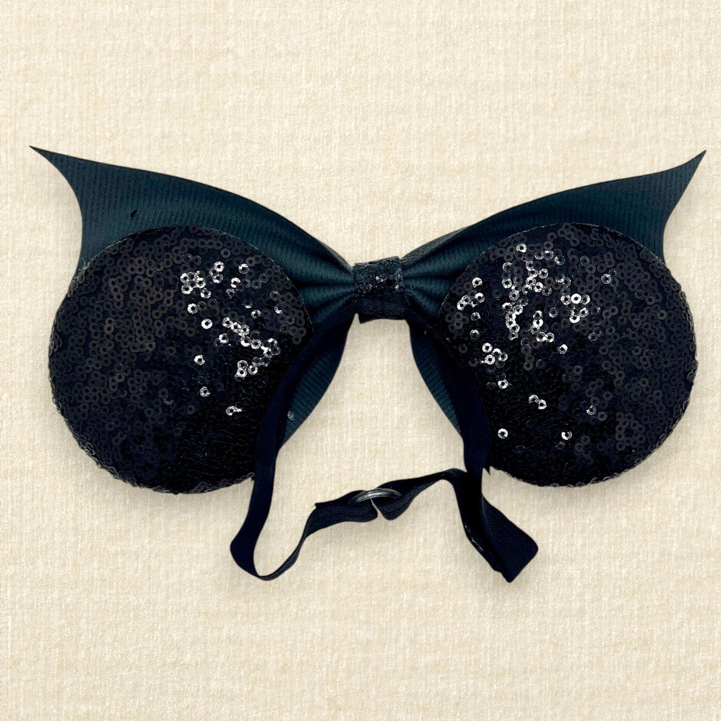 Halloween-themed mouse ears with black sequin ears, black glitter cobwebs, and black faux leather bat wing bow on an elastic headband (back view)