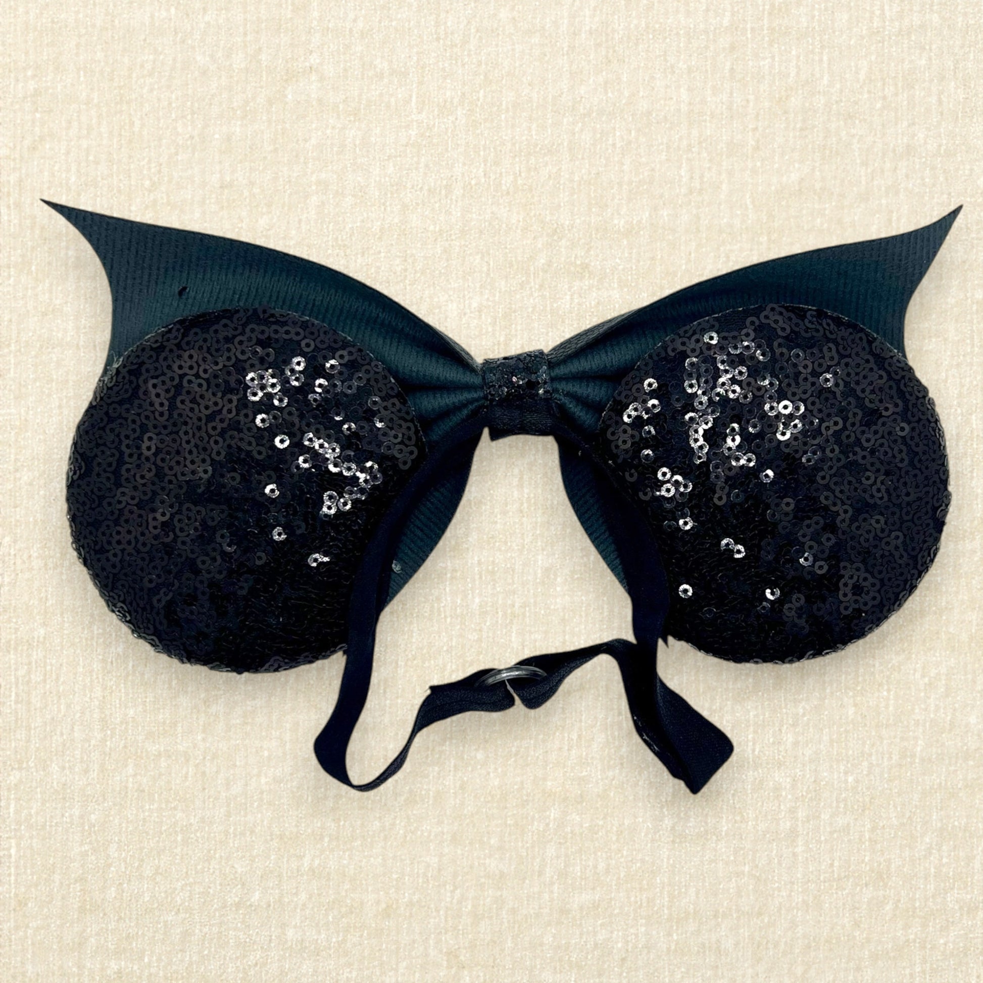 Halloween-themed mouse ears with black sequin ears, black glitter cobwebs, and black faux leather bat wing bow on an elastic headband (back view)
