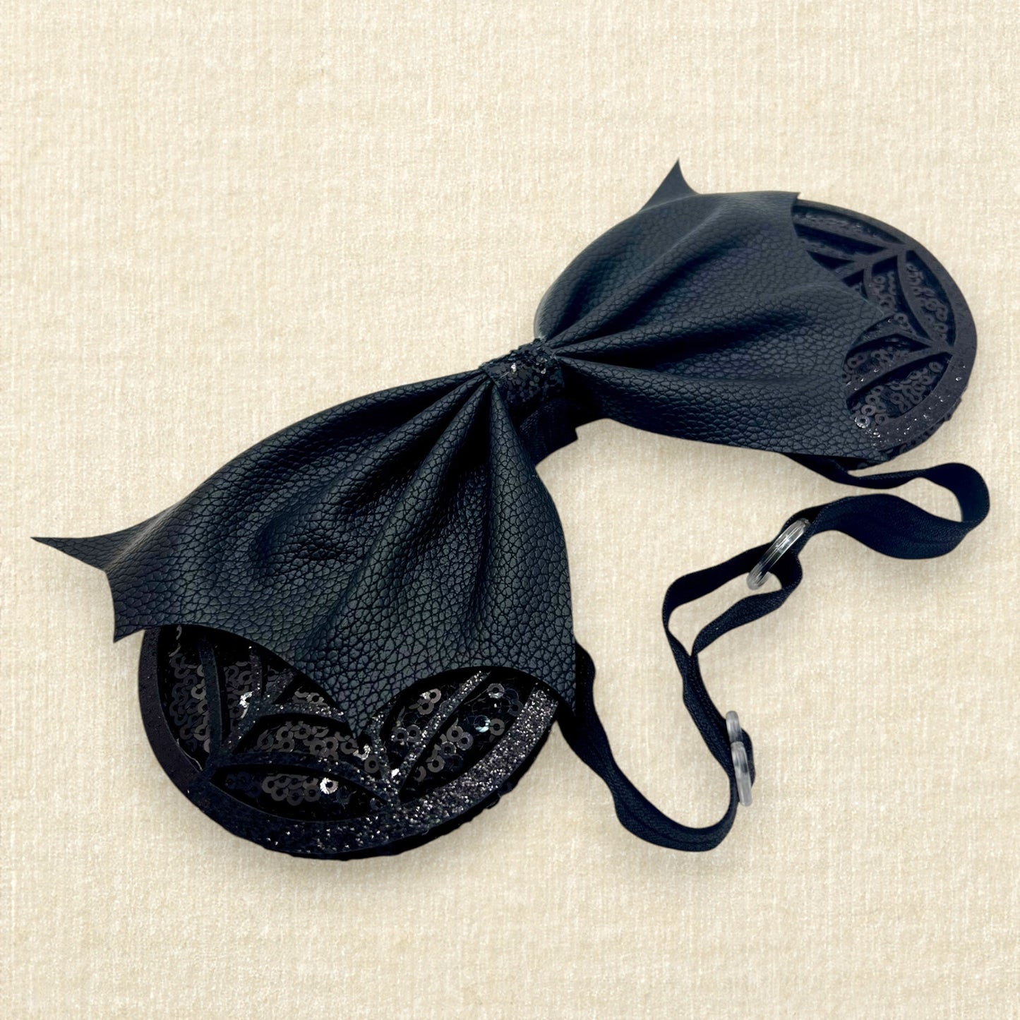 Halloween-themed mouse ears with black sequin ears, black glitter cobwebs, and black faux leather bat wing bow on an elastic headband