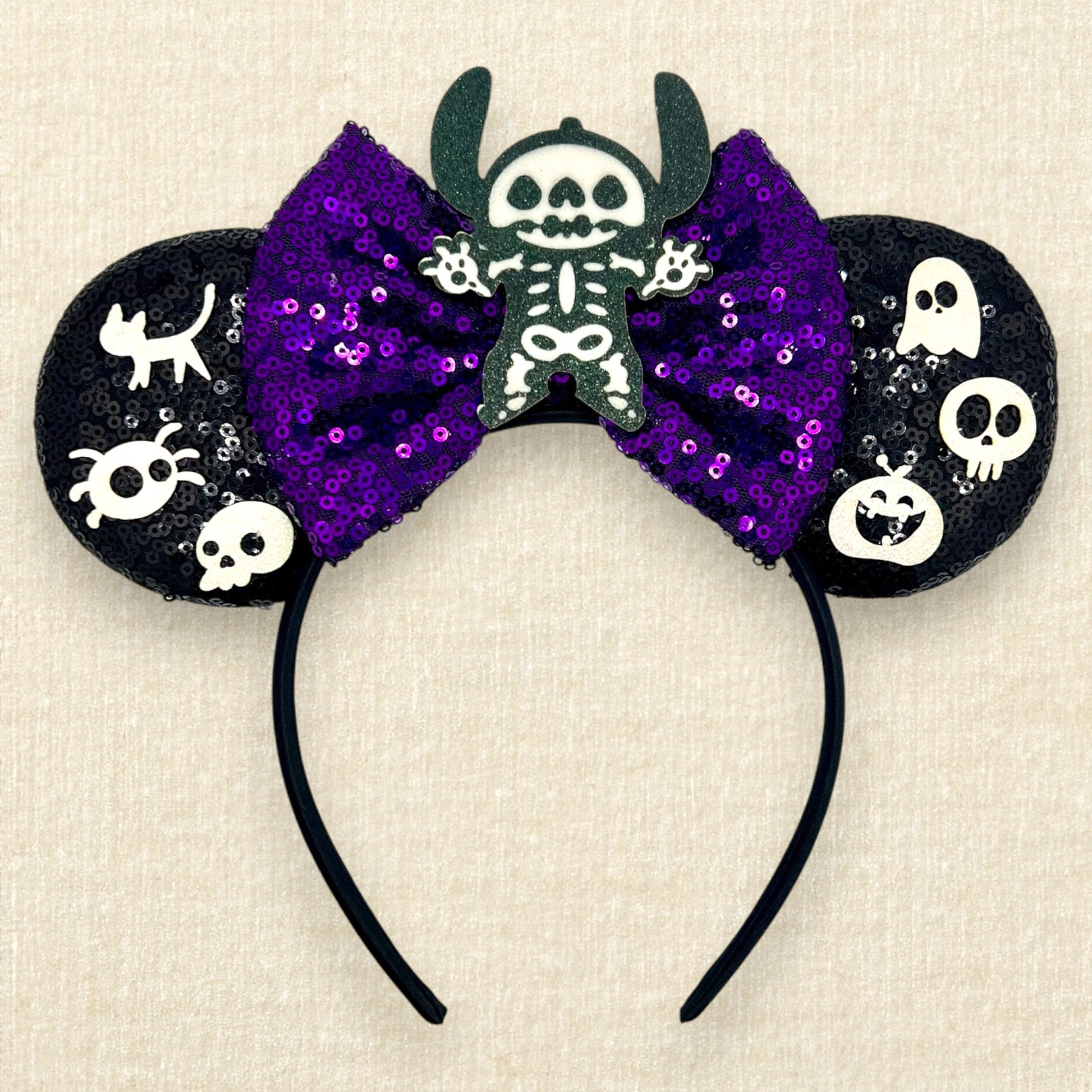 Halloween-themed black mouse ears headband with spooky glitter creatures, purple sequin bow, and skeleton Stitch centerpiece