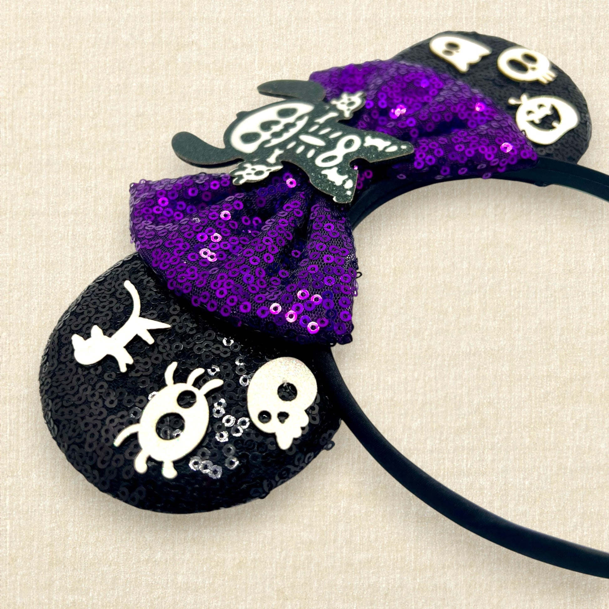 Halloween-themed black mouse ears headband with spooky glitter creatures, purple sequin bow, and skeleton Stitch centerpiece