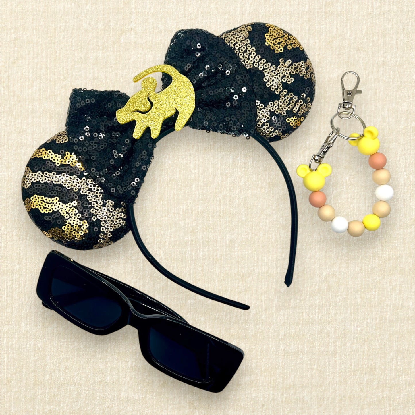 Black and gold sequin mouse ears in a leopard print pattern with a black sequin bow and gold glitter Simba accent; black sunglasses; yellow beaded mouse ears holder clip