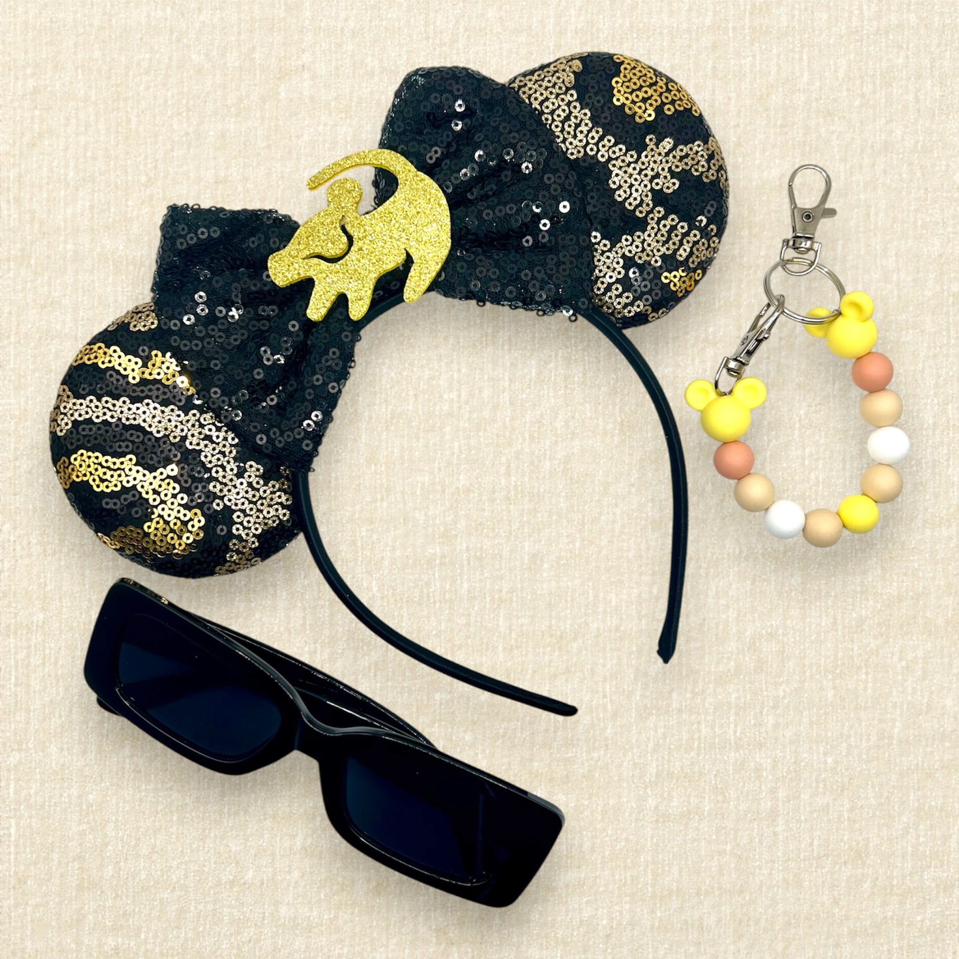 Black and gold sequin mouse ears in a leopard print pattern with a black sequin bow and gold glitter Simba accent; black sunglasses; yellow beaded mouse ears holder clip