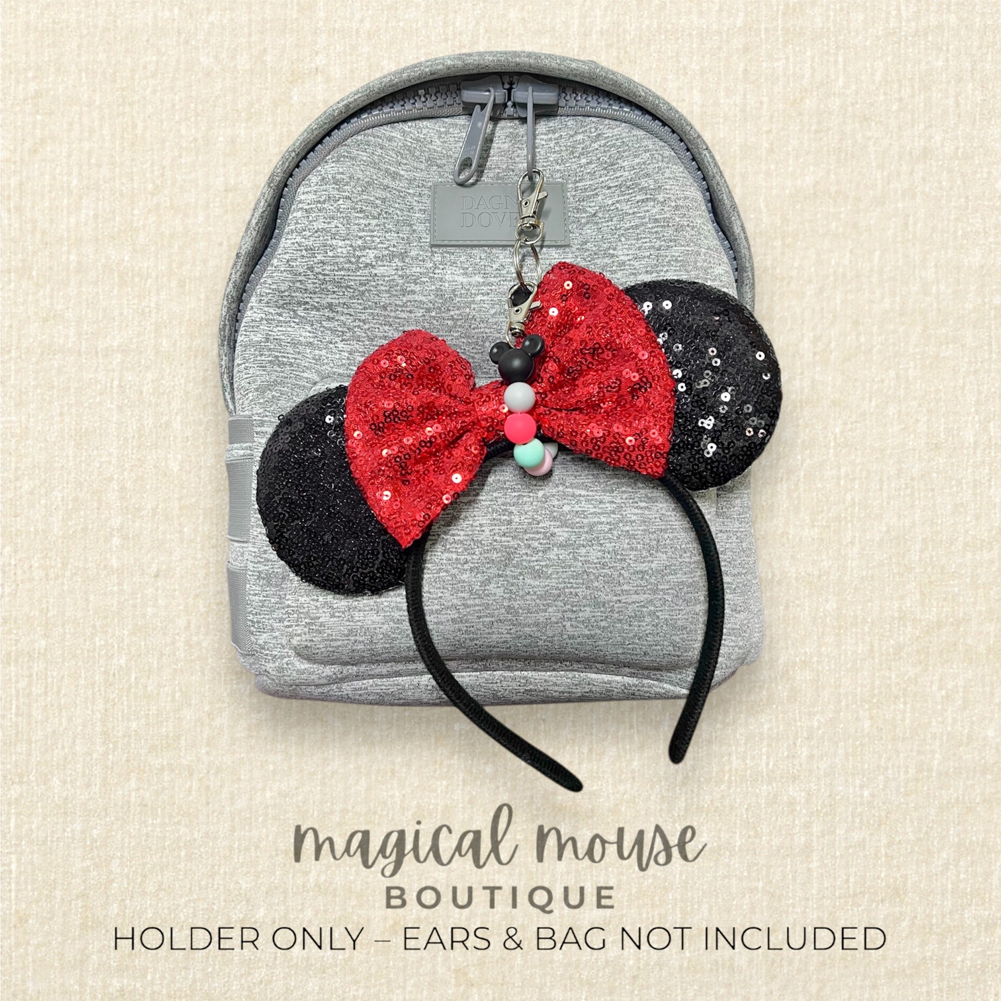 Red bow and black ears on a colorful beaded keychain on a gray backpack with 'magical mouse boutique' text.