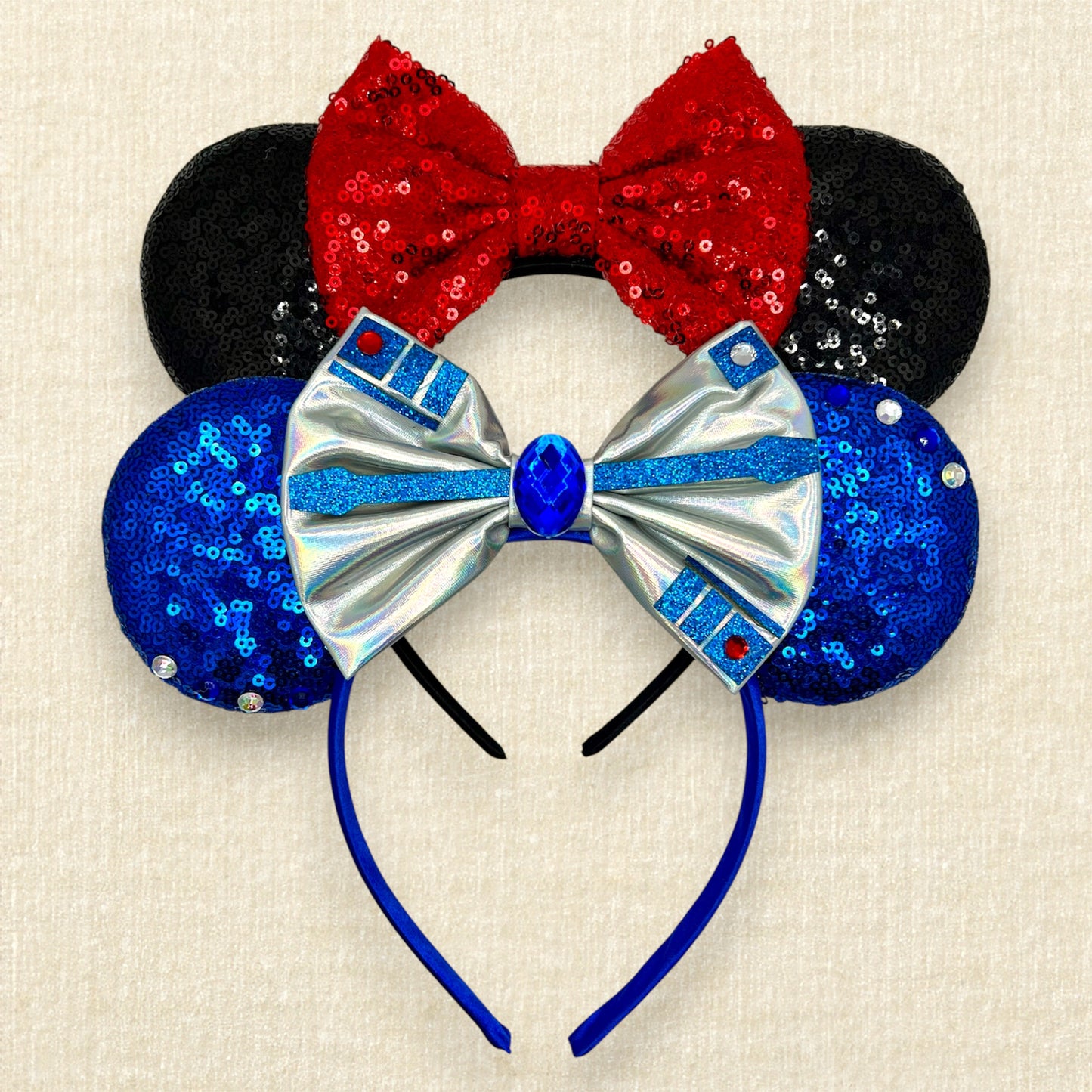 One pair of black mouse ears with red bow, and one pair of blue mouse ears with silver bow, rhinestones, and glitter accents.