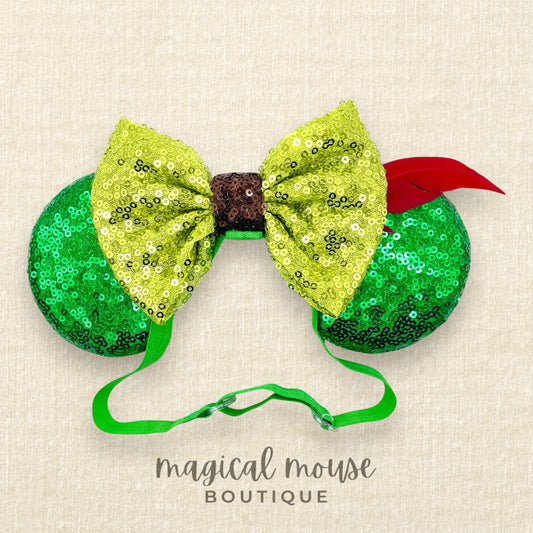 Green sequin elastic mouse ears  with lighter green sequin bow and red feather headband on a beige background, branded "Magical Mouse Boutique"