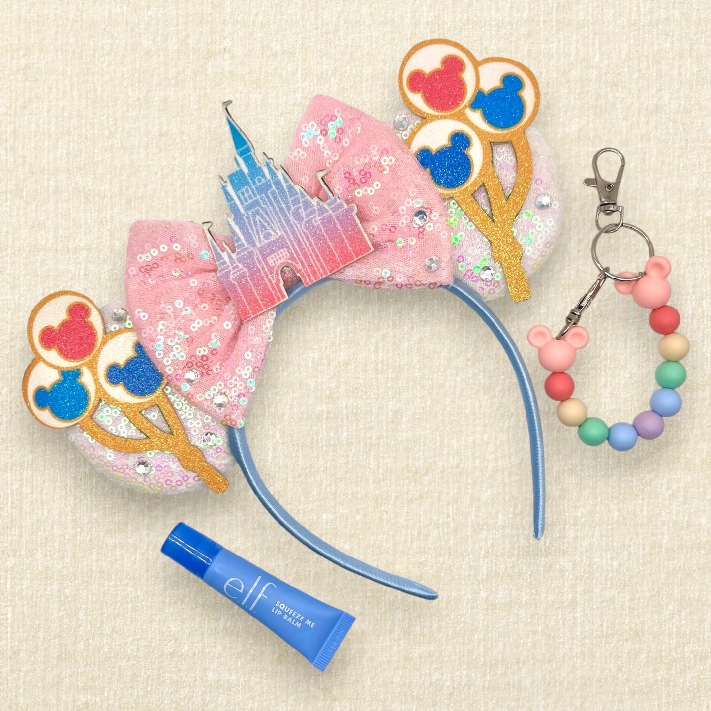 White sequin mouse ears with colorful mouse balloons and a pink bow with pastel pink and blue castle centerpiece; blue lip gloss tube; colorful beaded mouse ears holder