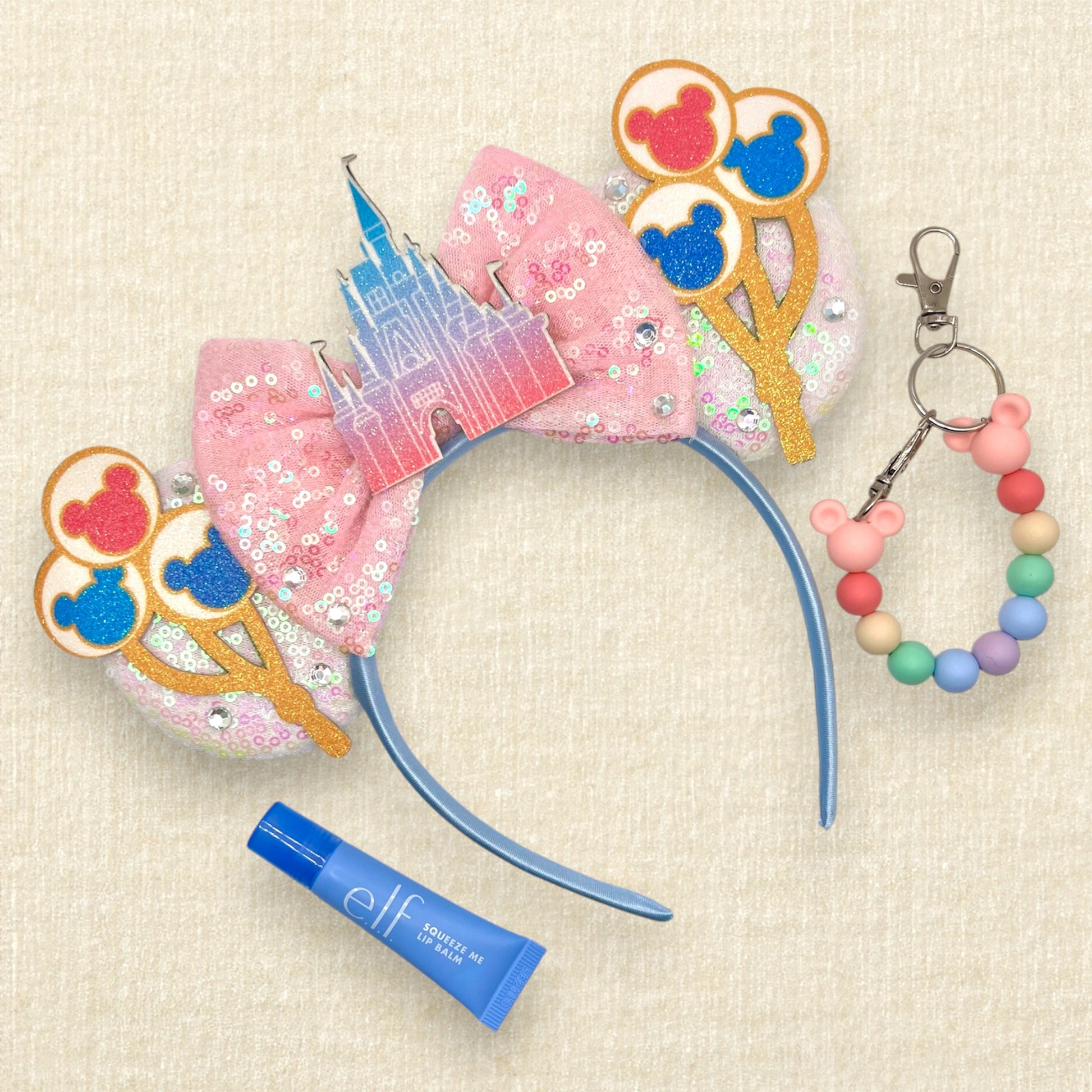 White sequin mouse ears with colorful mouse balloons and a pink bow with pastel pink and blue castle centerpiece; blue lip gloss tube; colorful beaded mouse ears holder