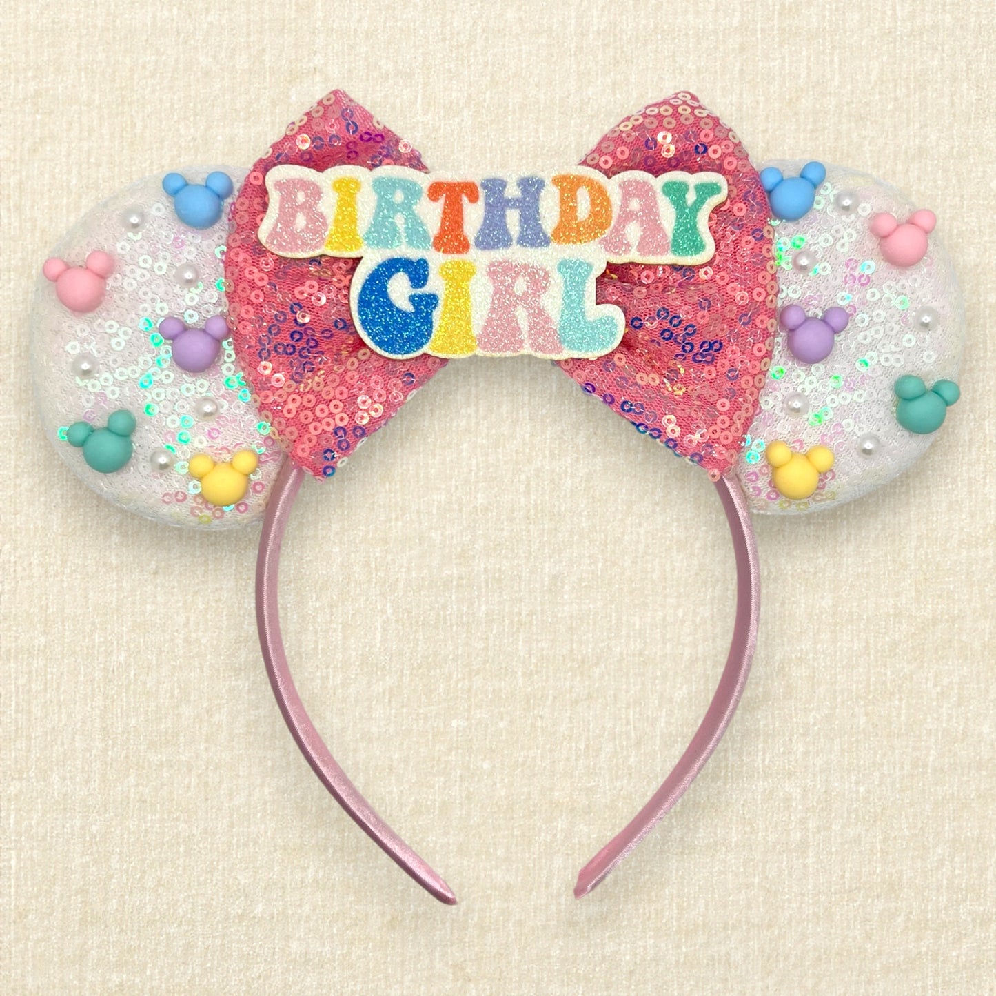 Iridescent white mouse ears with colorful mouse pearls, a pink sequin bow, and glitter "Birthday Girl" text centerpiece