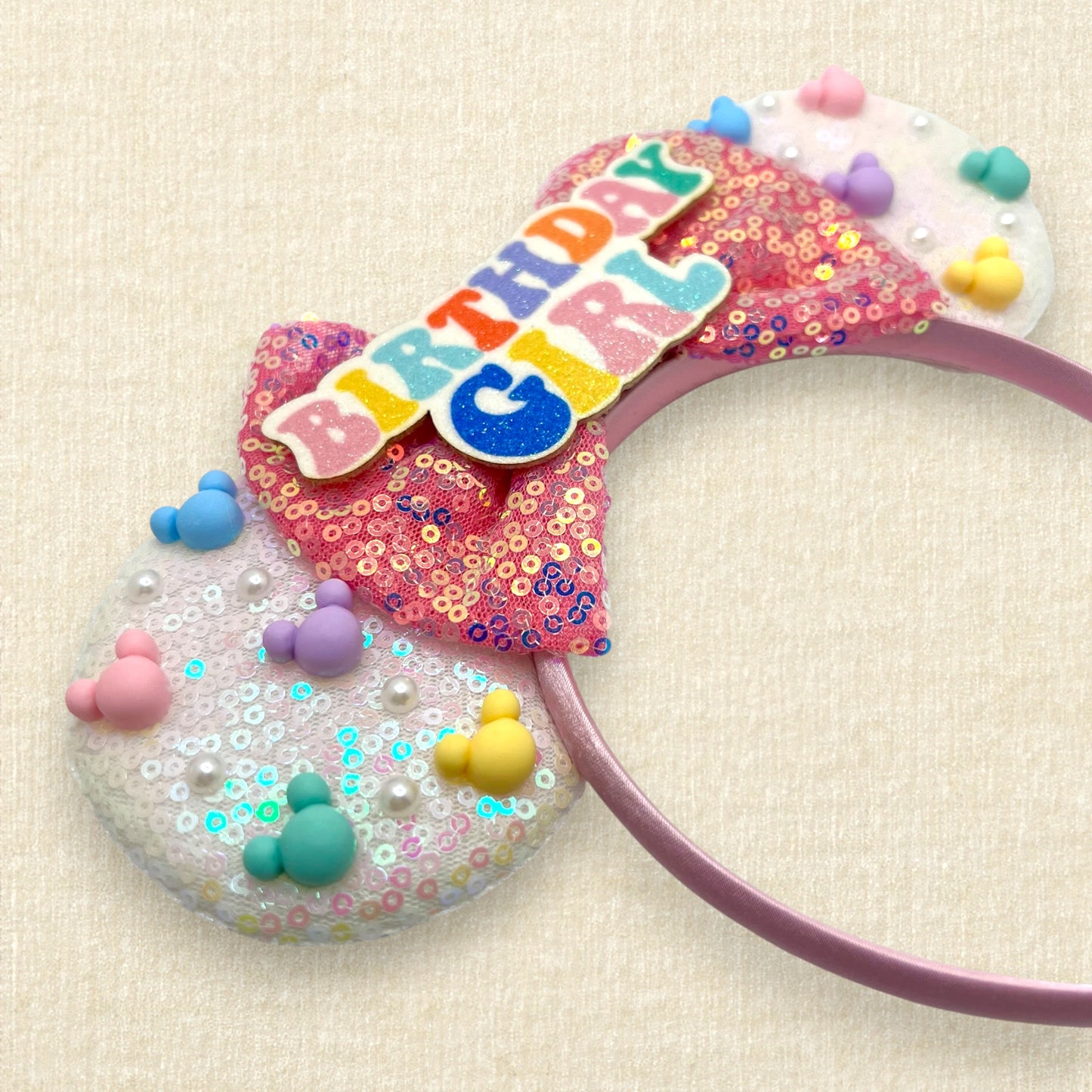 Iridescent white mouse ears with colorful mouse pearls, a pink sequin bow, and glitter "Birthday Girl" text centerpiece