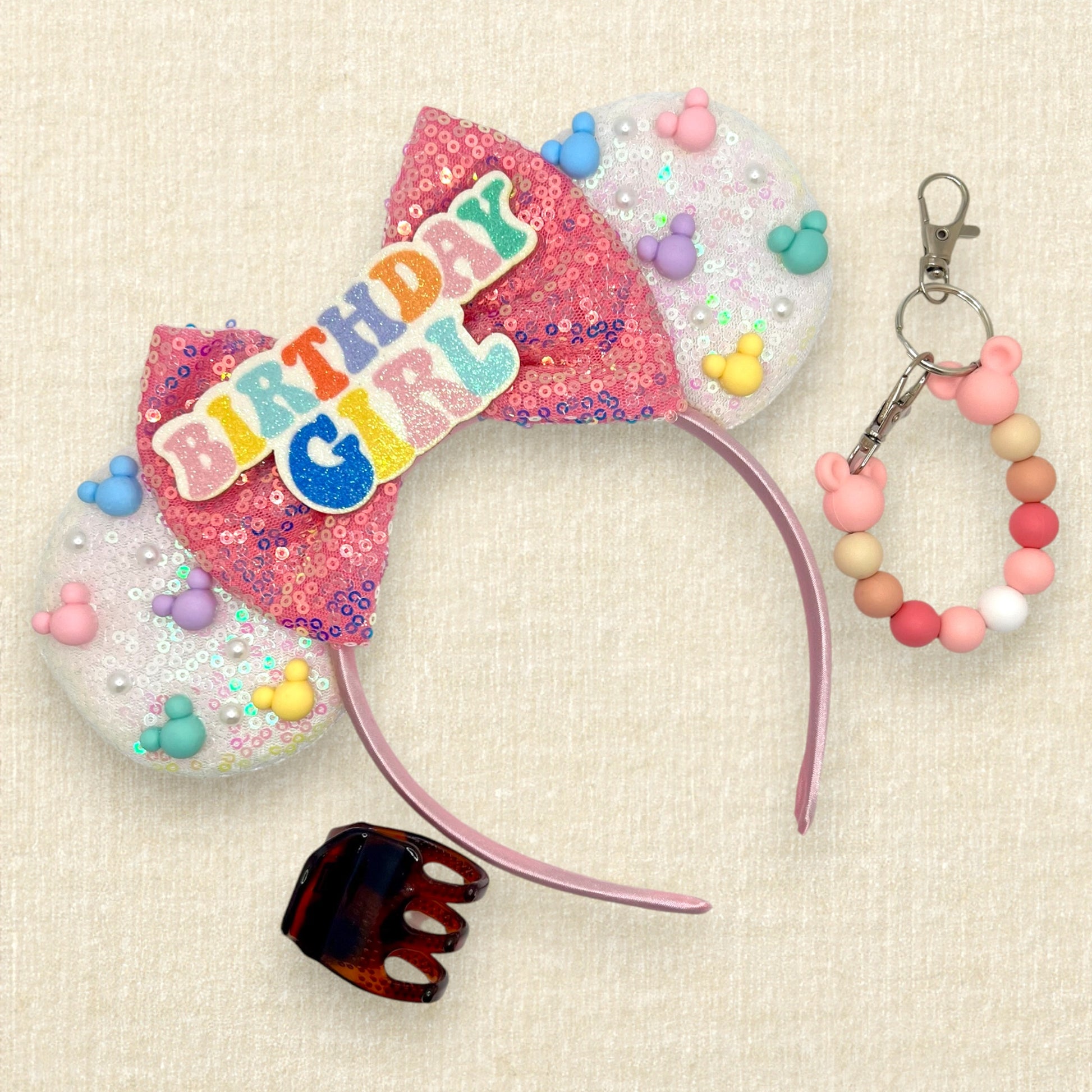 Iridescent white mouse ears with colorful mouse pearls, a pink sequin bow, and glitter "Birthday Girl" text centerpiece; tortoiseshell claw clip; pink and white beaded mouse ears holder keychain