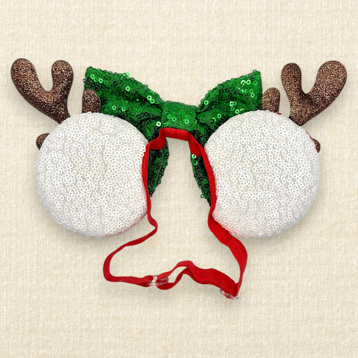 Christmas-themed mouse ears headband with a large green sequined bow, brown reindeer antlers, and candy cane side mouse ears in red and white stripes, shown on a light beige textured background (Back view)