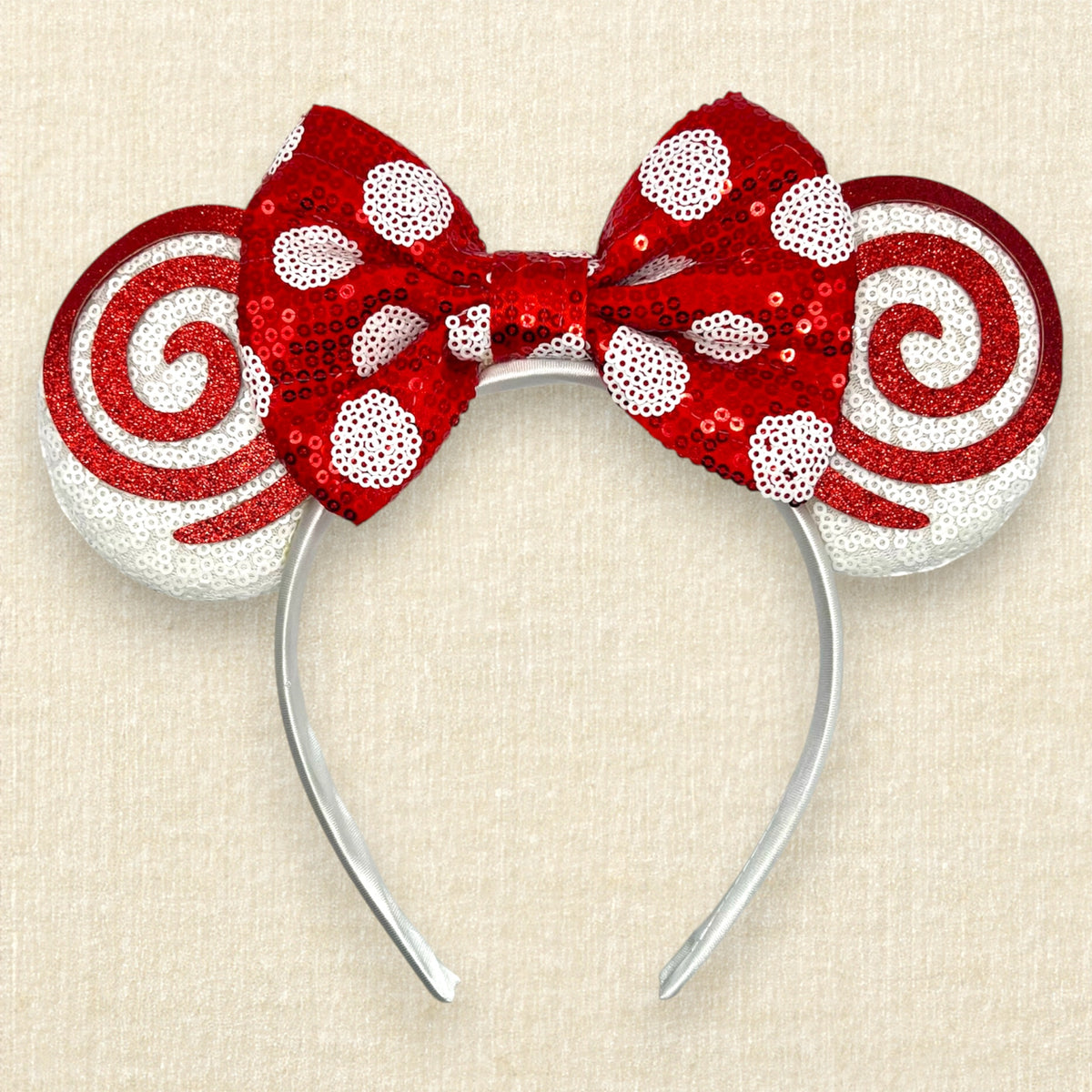 A Christmas mouse ears headband with white sequin ears, red glitter swirls, and a red sequin bow with white polka dots.