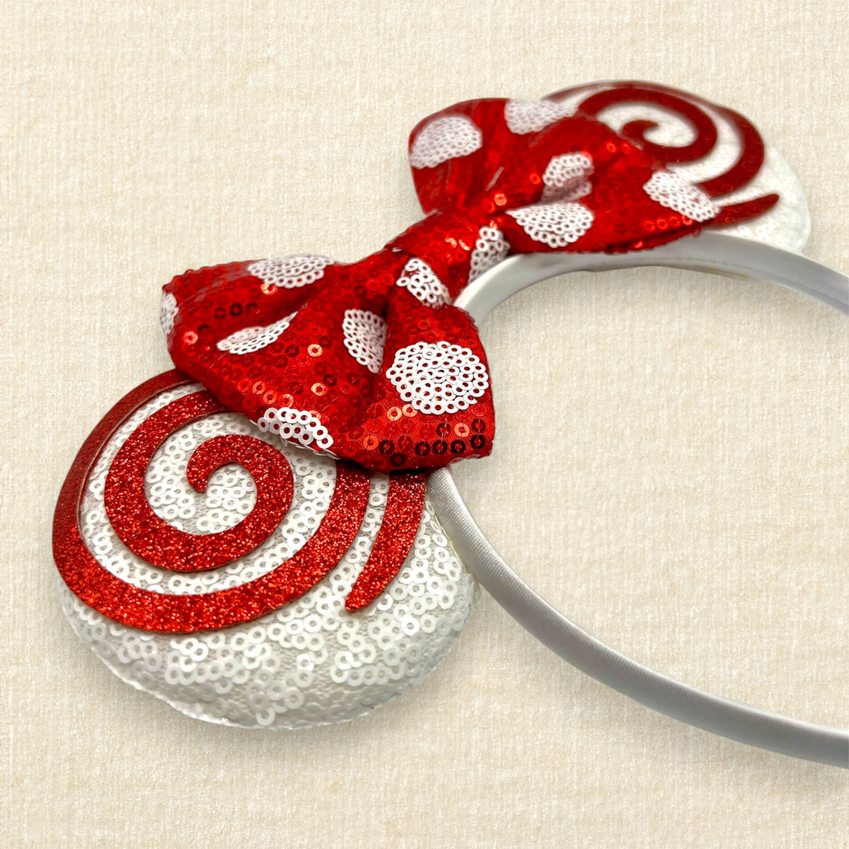 A Christmas mouse ears headband with white sequin ears, red glitter swirls, and a red sequin bow with white polka dots.