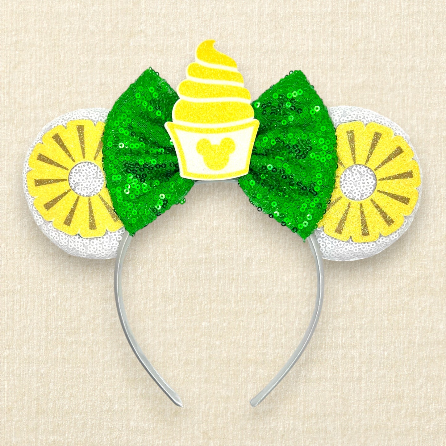 White mouse ears with glitter pineapple rings, green bow, and cup of pineapple swirl soft serve