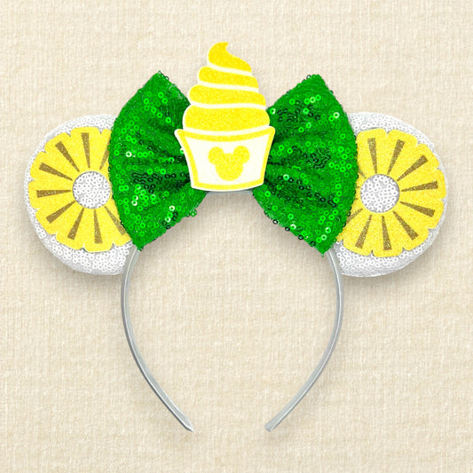 White mouse ears with glitter pineapple rings, green bow, and cup of pineapple swirl soft serve
