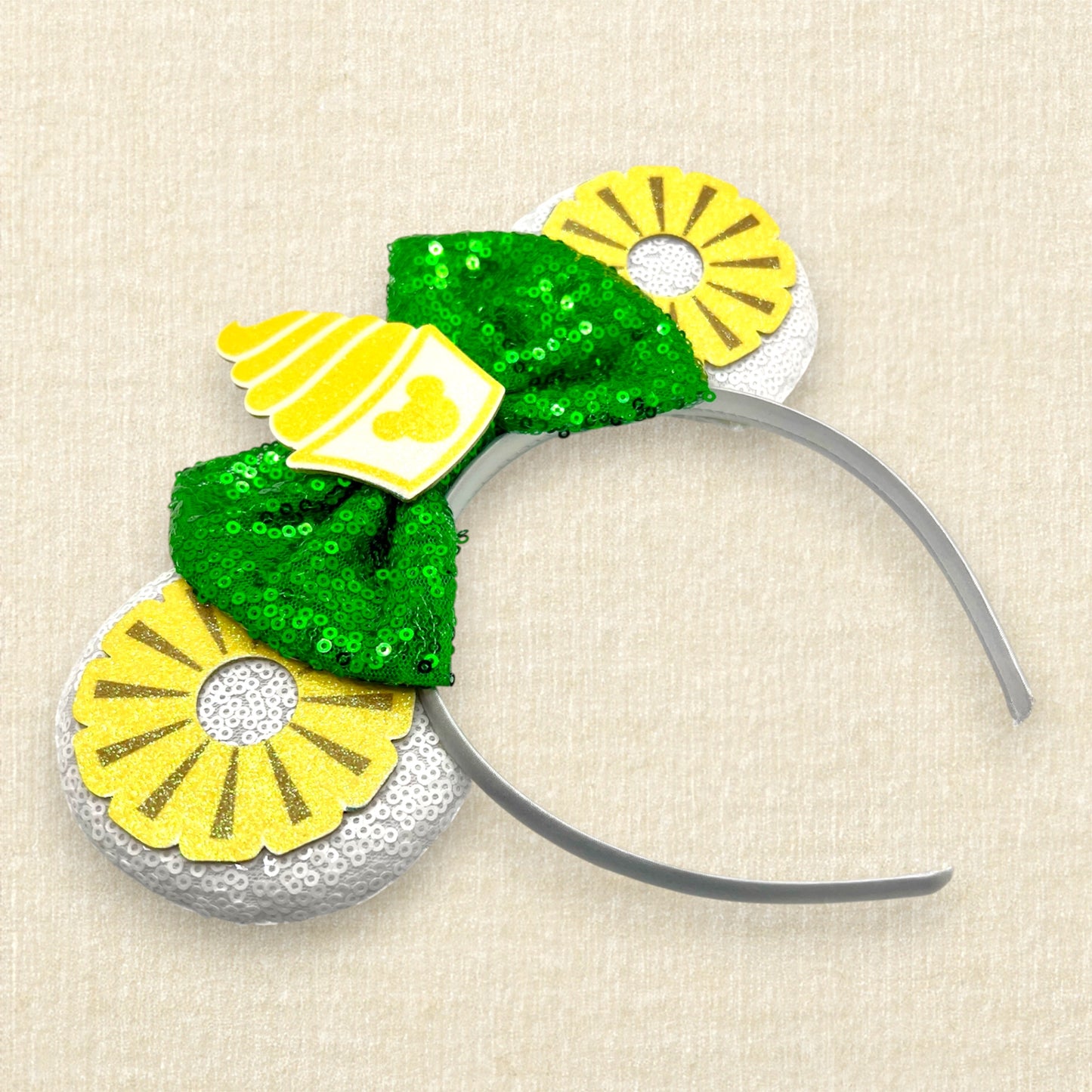 White mouse ears with glitter pineapple rings, green bow, and cup of pineapple swirl soft serve