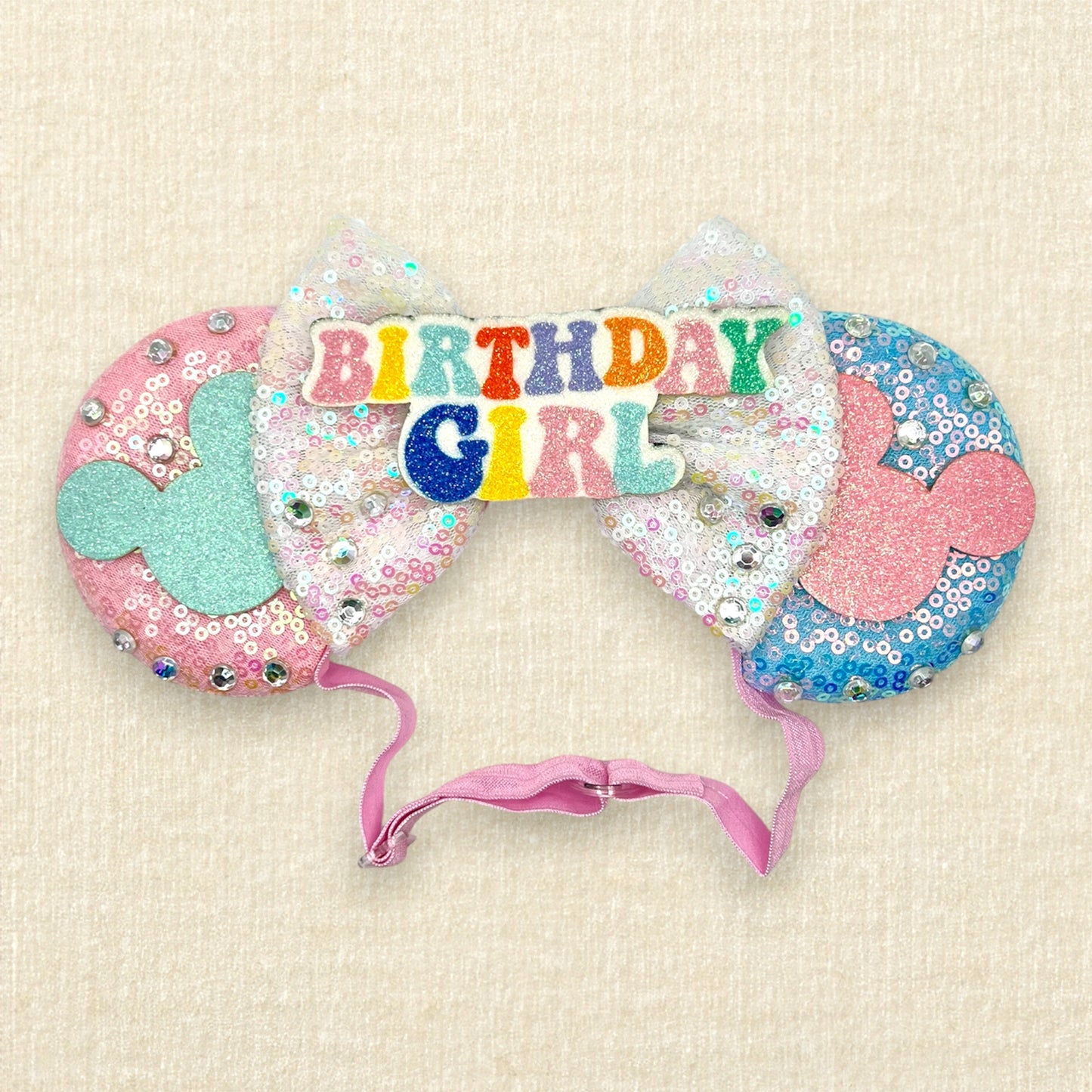 Pink and blue mouse ears with glitter mouse silhouettes, iridescent white sequin bow, and "Birthday Girl" text centerpiece