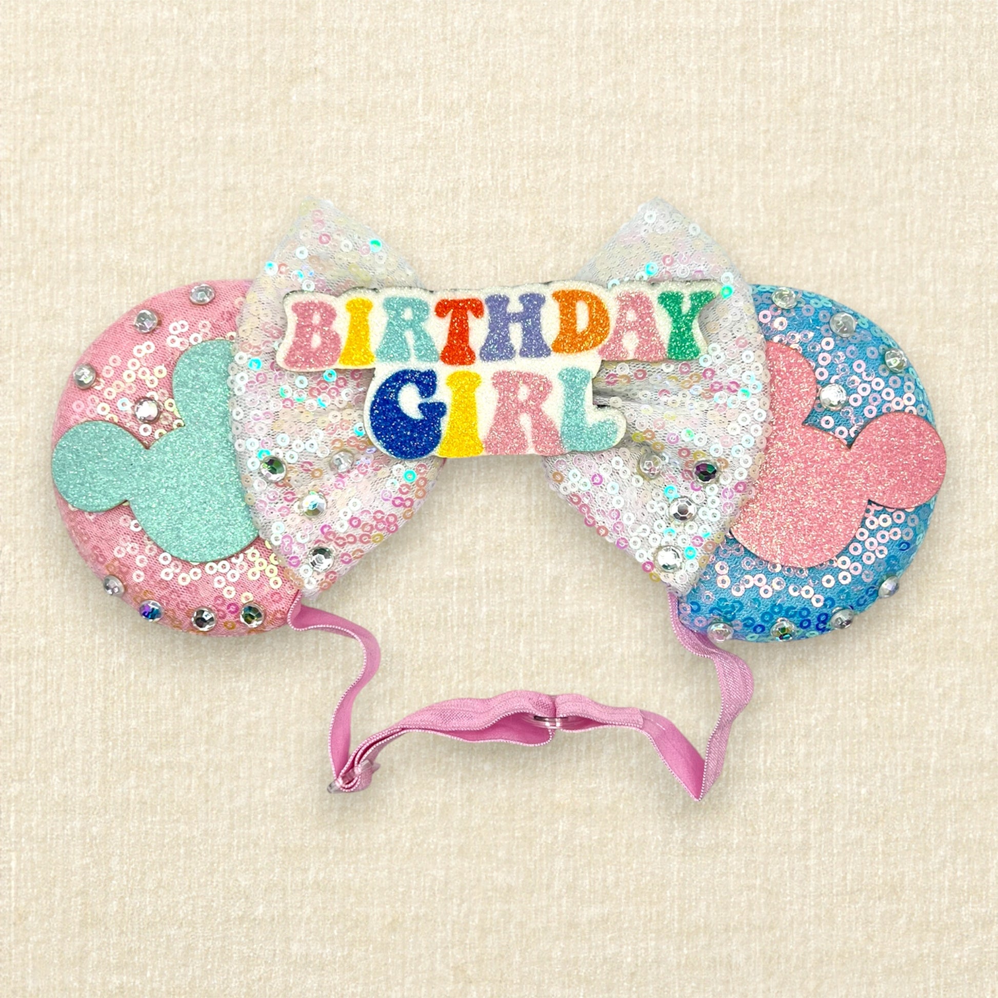 Pink and blue mouse ears with glitter mouse silhouettes, iridescent white sequin bow, and "Birthday Girl" text centerpiece