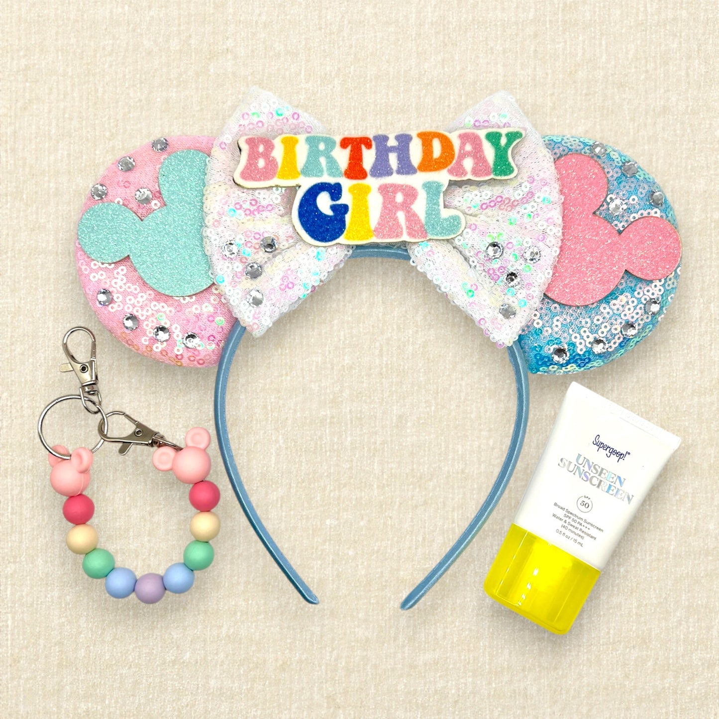 Pink and blue mouse ears with mouse silhouettes, white sequin bow, and colorful "Birthday Girl" text; colorful beaded mouse ears holder; sunblock