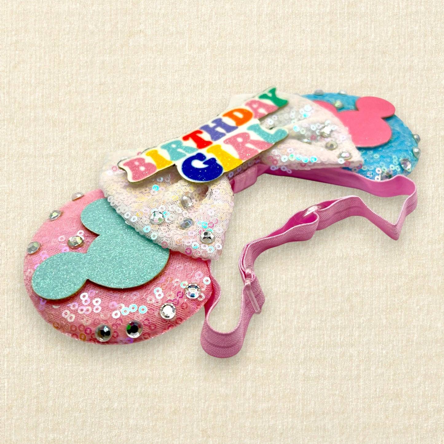 Pink and blue mouse ears with glitter mouse silhouettes, iridescent white sequin bow, and "Birthday Girl" text centerpiece