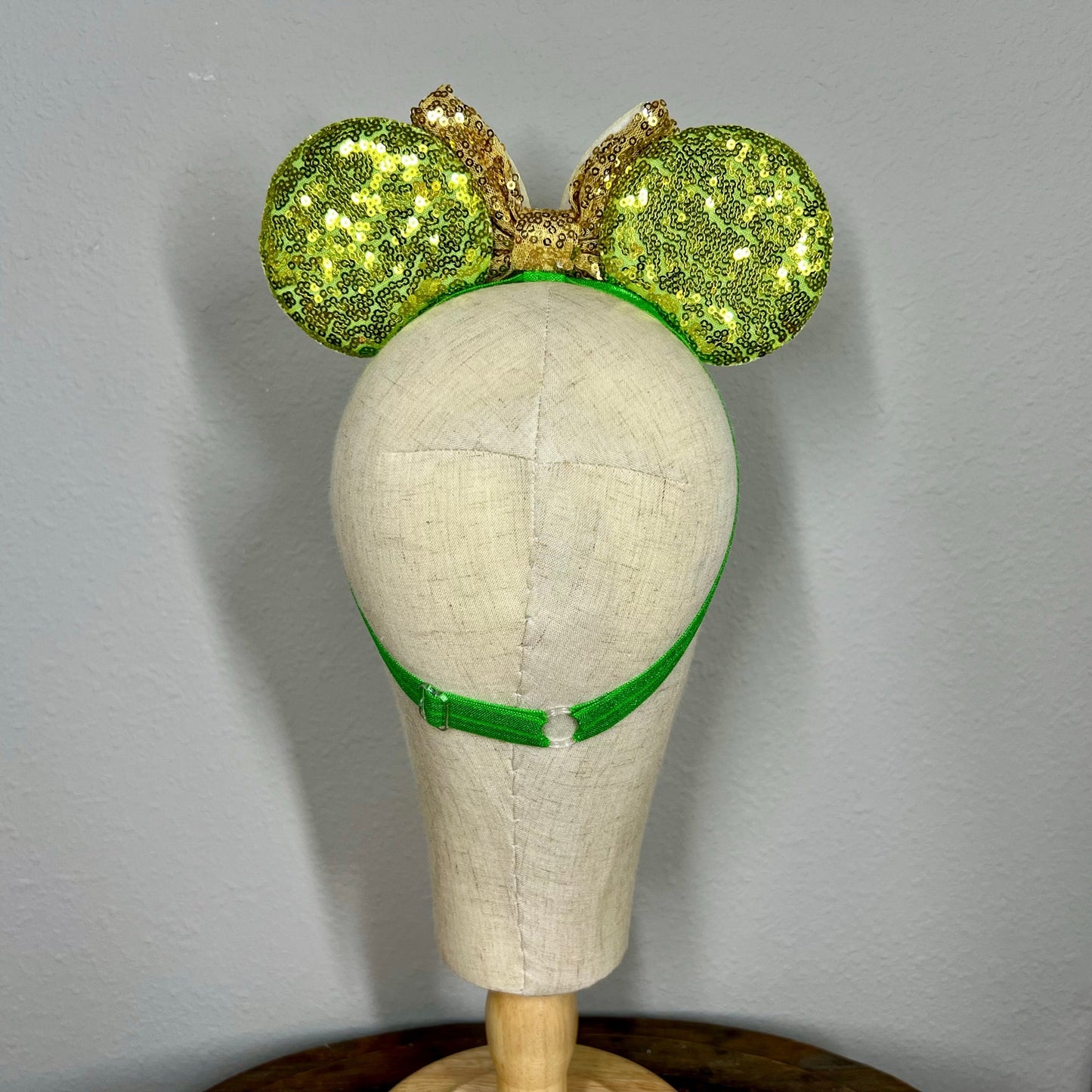 Green sequin mouse ears headband with gold bow and glitter fairy wings on a mannequin
