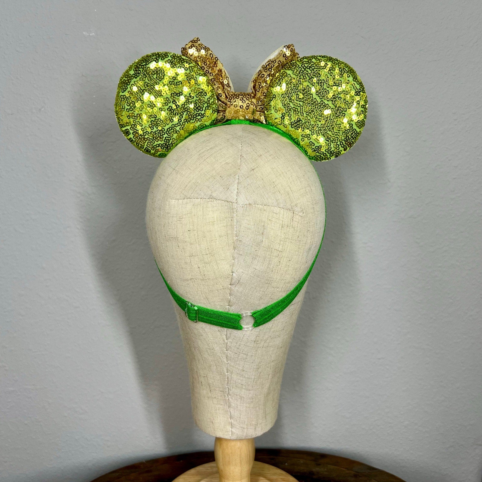 Green sequin mouse ears headband with gold bow and glitter fairy wings on a mannequin