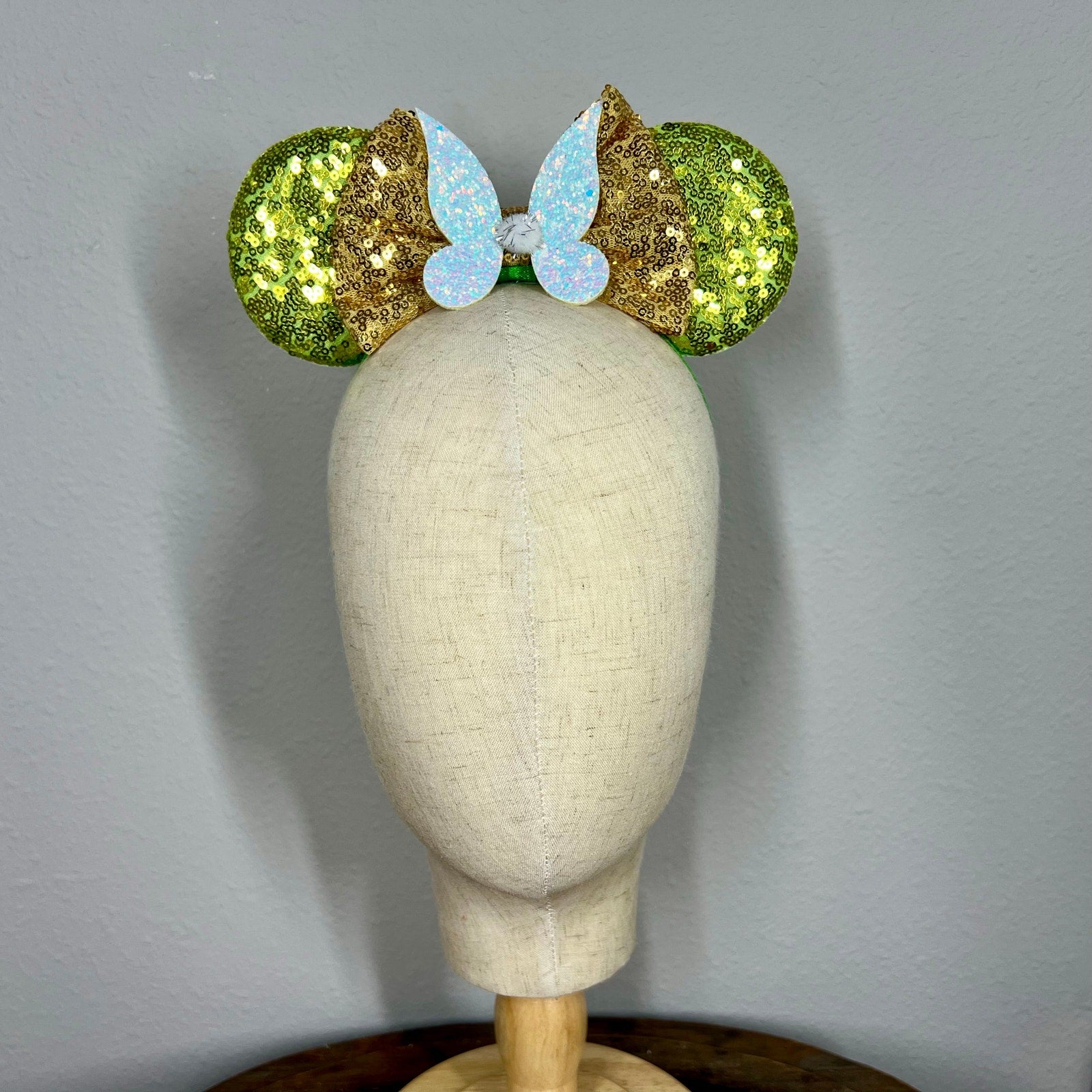 Green sequin mouse ears headband with gold bow and glitter fairy wings on a mannequin